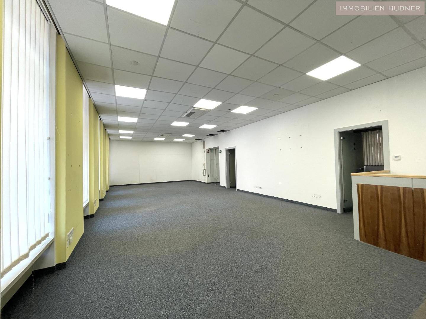 Weitläufiger, leerer Bürobereich mit Teppichboden, Rasterdecke und einem Empfangstresen.