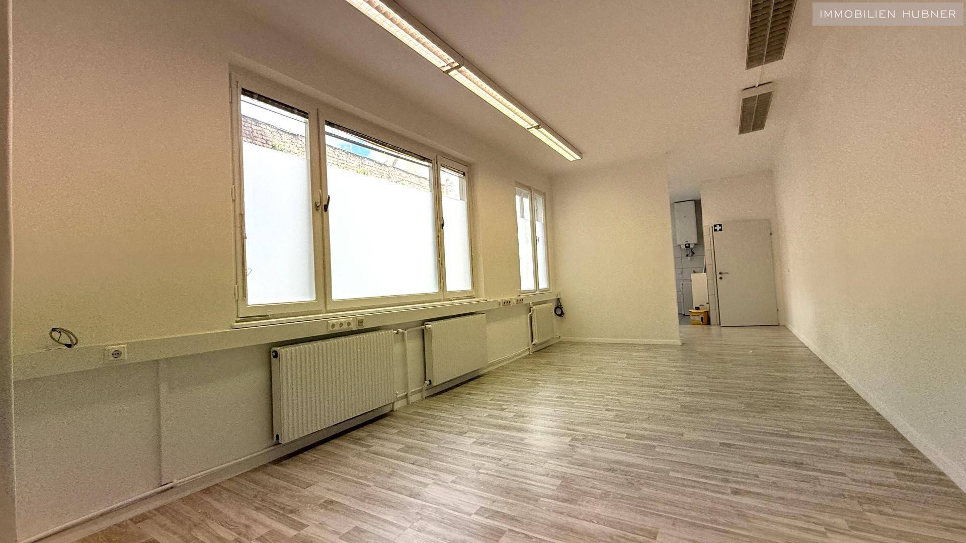 Heller Büroraum mit großen Fenstern, die viel Tageslicht hereinlassen, und einem modernen Laminatboden.