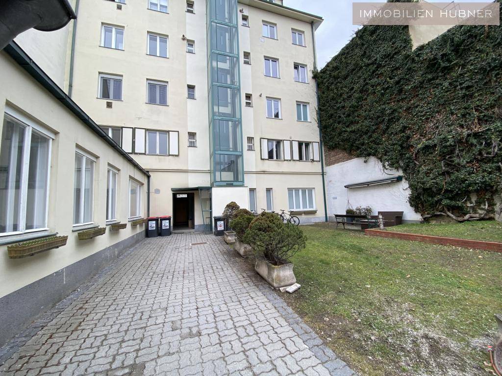 Gesamtansicht des Innenhofs mit gepflastertem Bereich, Grünfläche und dem Gebäude mit Außenaufzug.