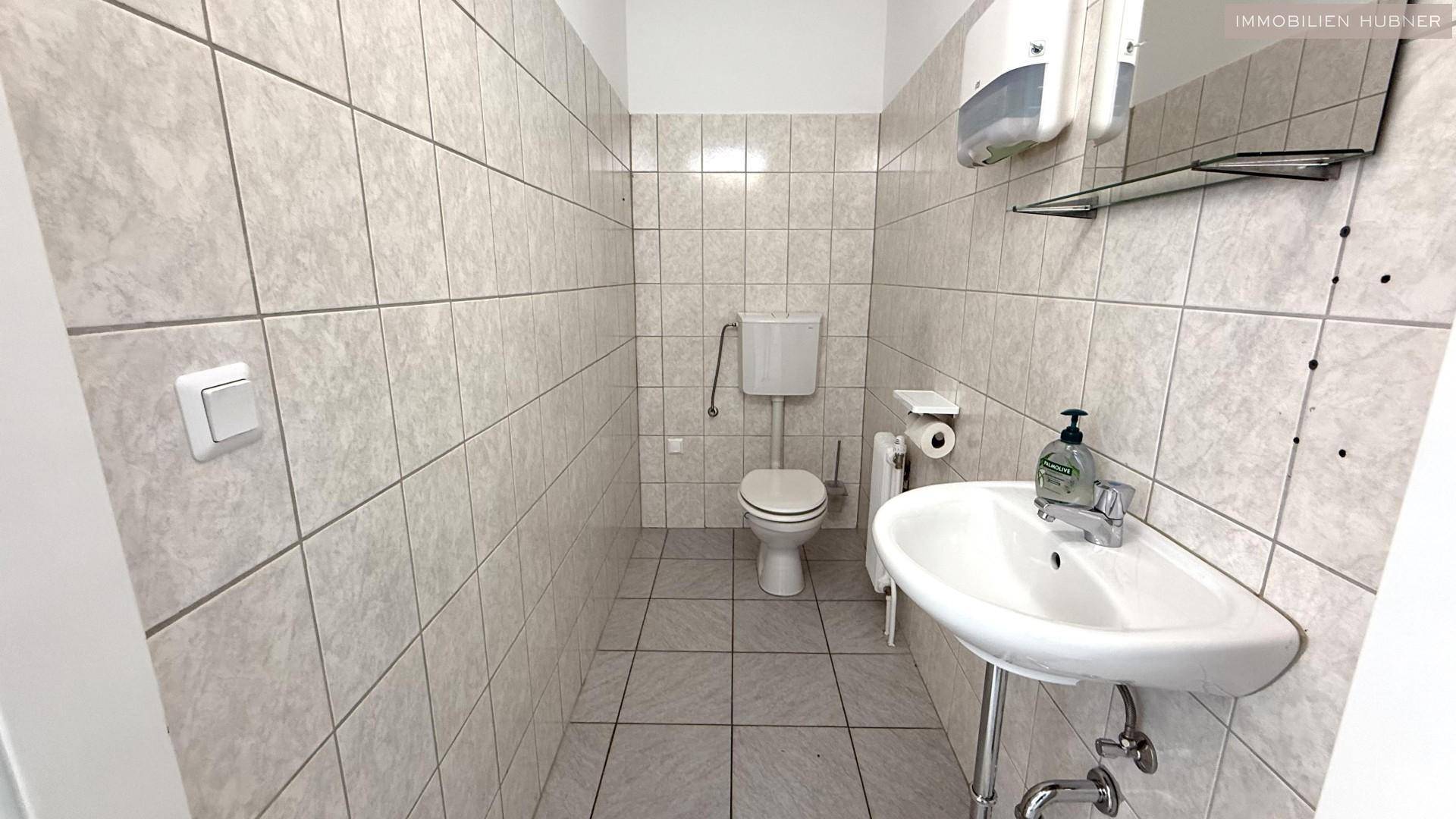Geflieste Toilette mit WC, Waschbecken und Seifenspender, in einem sauberen und funktionalen Zustand.