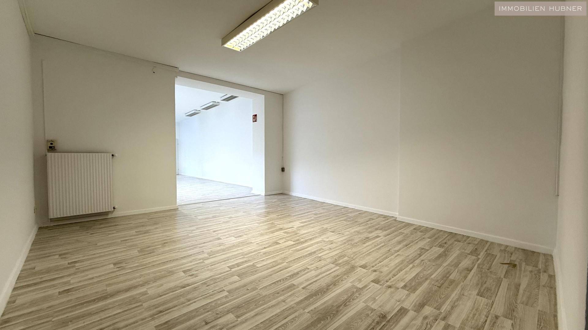 Weiterer Blick in einen hellen Büroraum mit Laminatboden und einem Durchgang zu einem anderen Bereich.