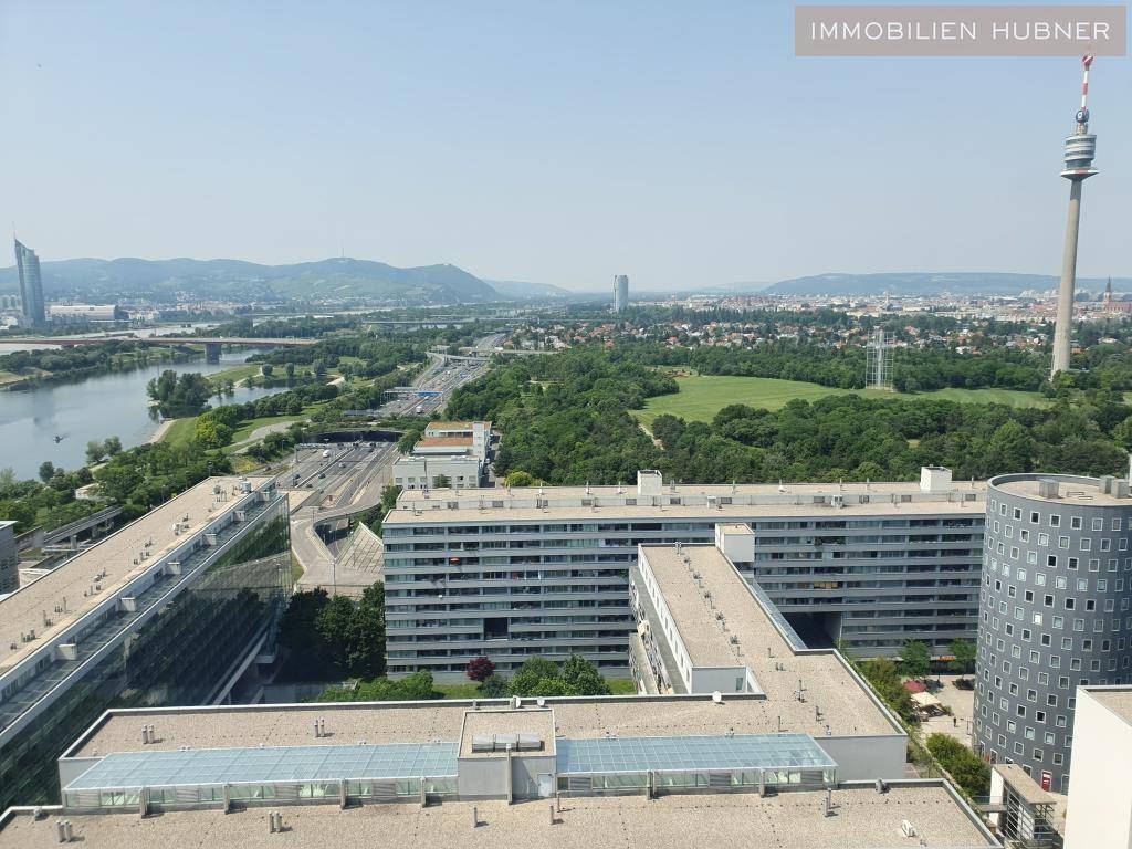 Weitläufiger Panoramablick über die Stadt mit Fluss, Grünflächen und markanten Gebäuden unter blauem Himmel.