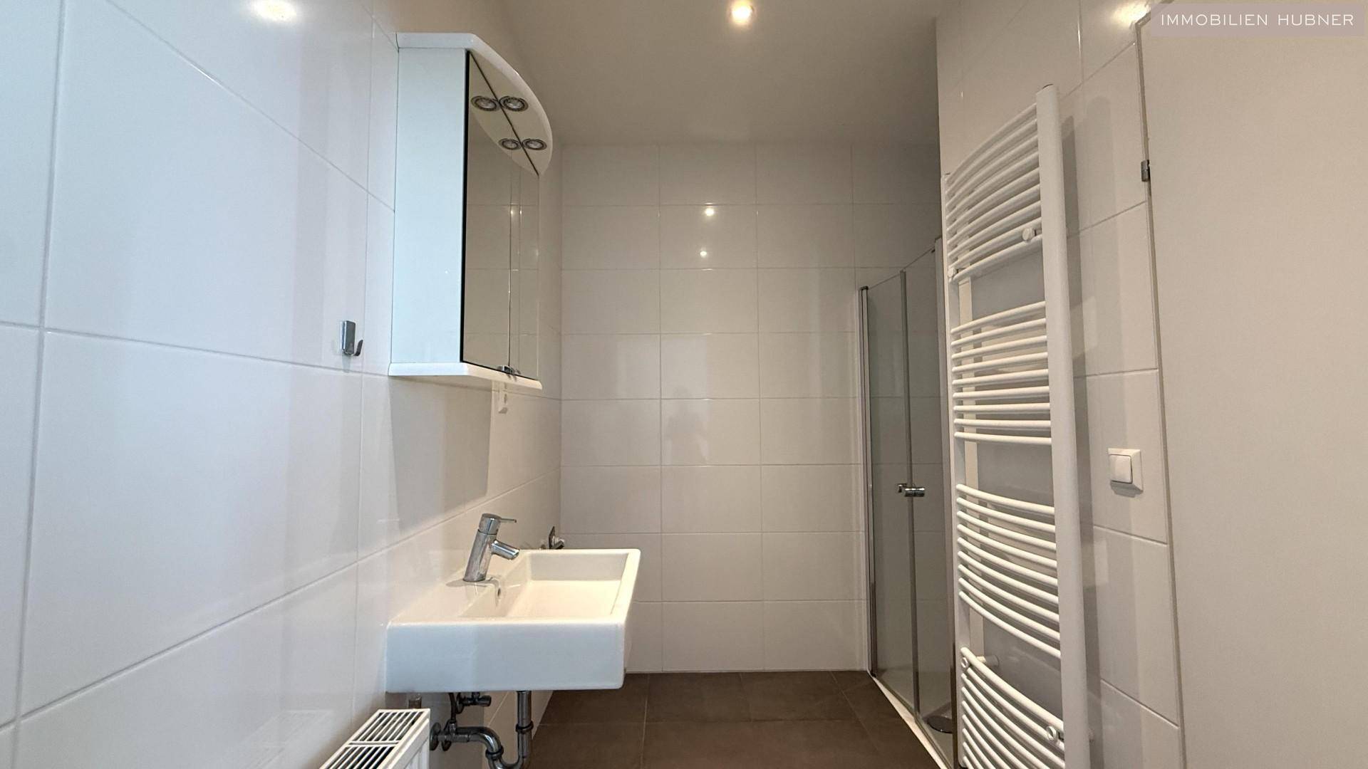 Helles Badezimmer mit weiß gefliesten Wänden, Waschbecken und Duschkabine.