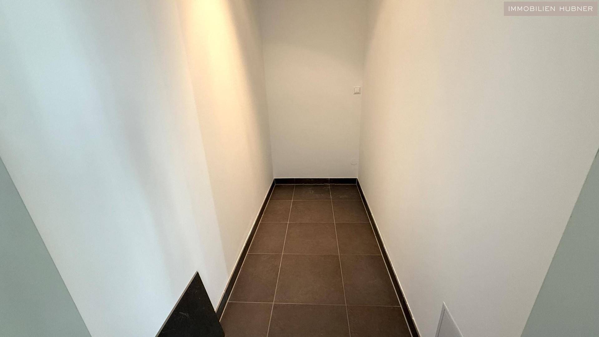 Schmaler Flur mit Fliesenboden und weißen Wänden, gut beleuchtet.