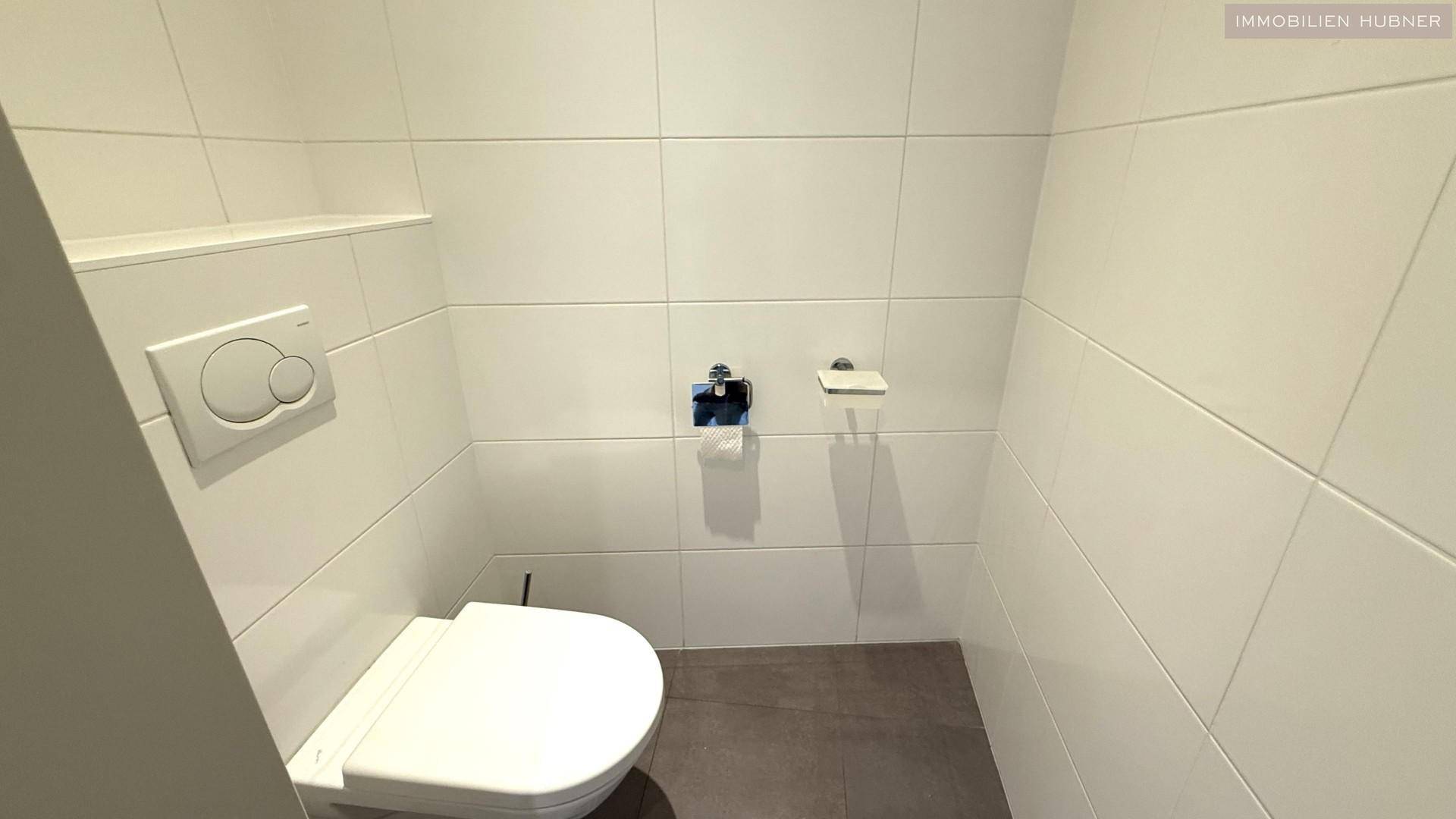 Separate Toilette mit wandhängendem WC und weißen Fliesen an den Wänden.