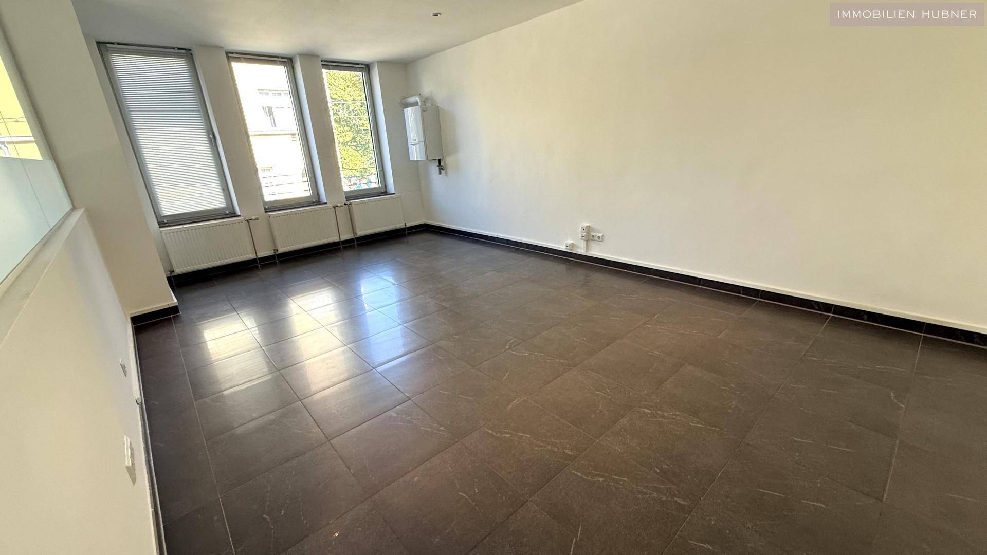 Leerer Büroraum mit Fliesenboden, Heizkörpern und einem Wandanschluss.