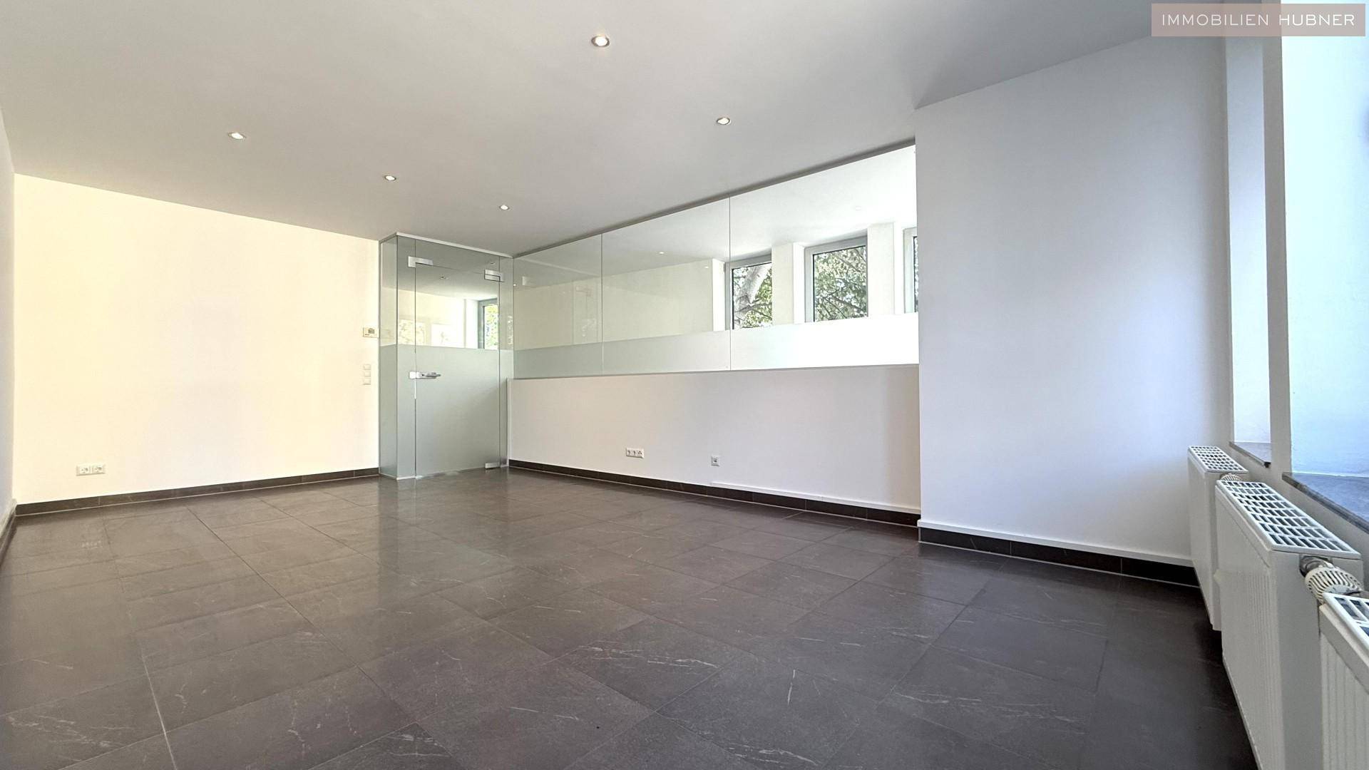 Heller Büroraum mit großen Fenstern, Fliesenboden und einer eleganten Glaswand.