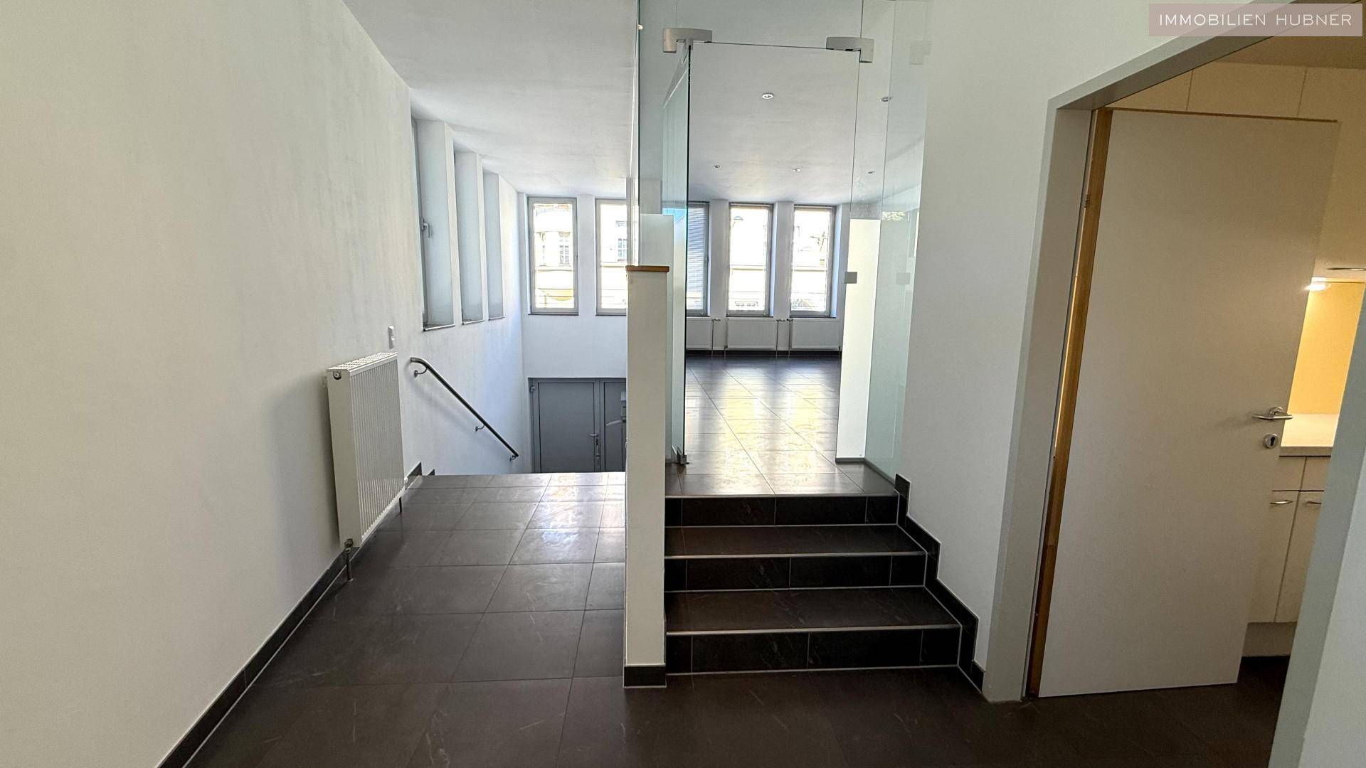 Eingangsbereich mit Treppe, Fliesenboden und Glasgeländer, führt zu weiteren Räumen.