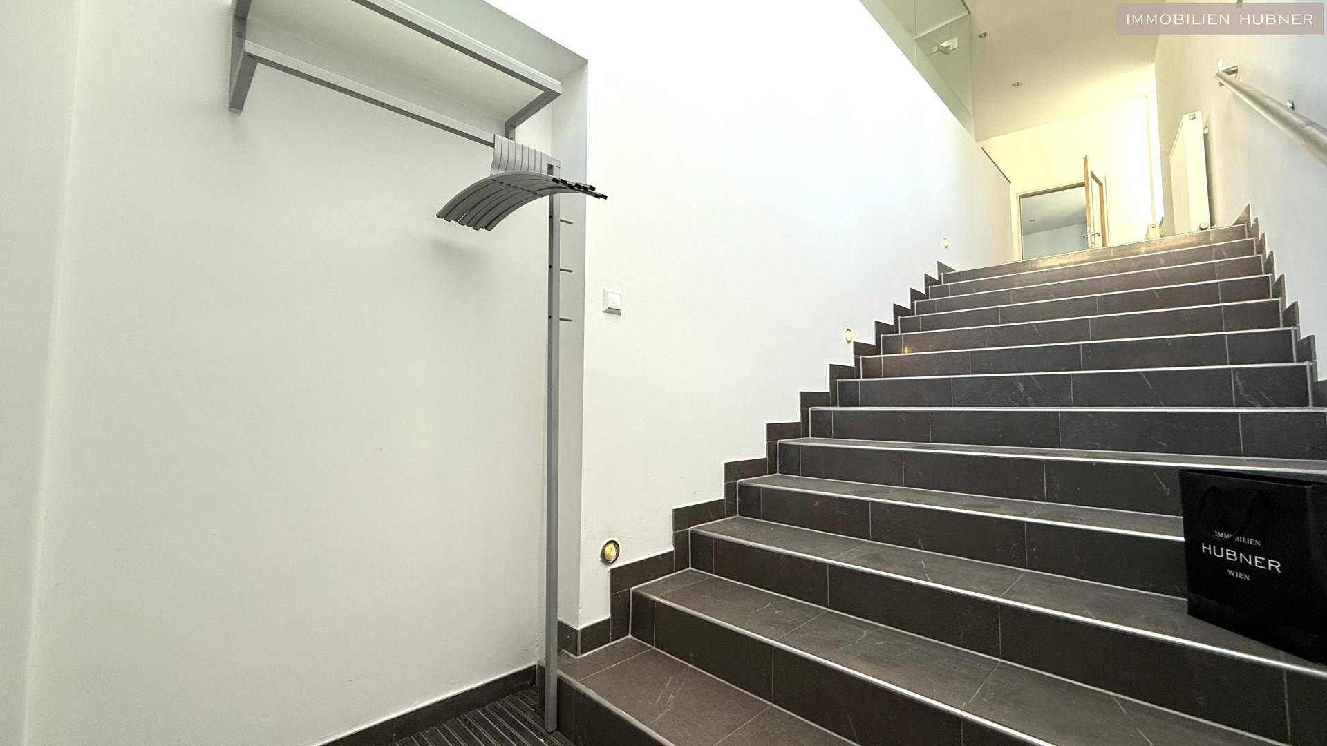 Treppenhaus mit dunklen Fliesenstufen und einem modernen Geländer.