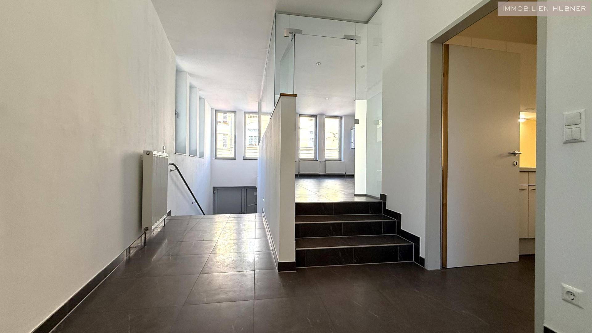 Flur mit Treppe, Fliesenboden und Glasabtrennung, bietet Zugang zu verschiedenen Bereichen.
