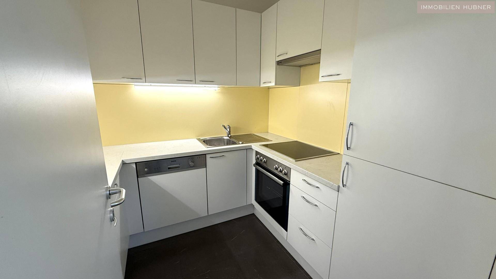 Moderne Einbauküche mit weißen Schränken, Spülmaschine und Kochfeld.