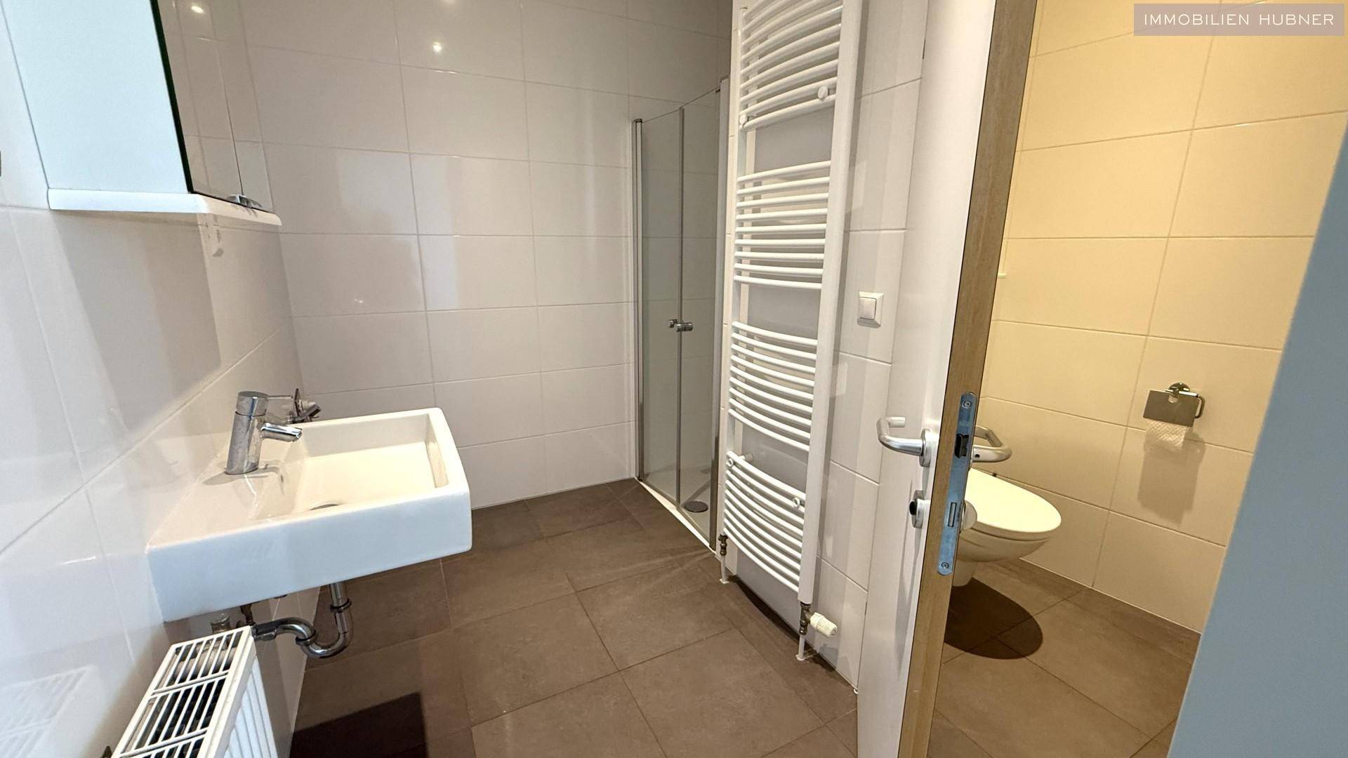 Modernes Badezimmer mit Waschbecken, Duschkabine und Handtuchheizkörper.