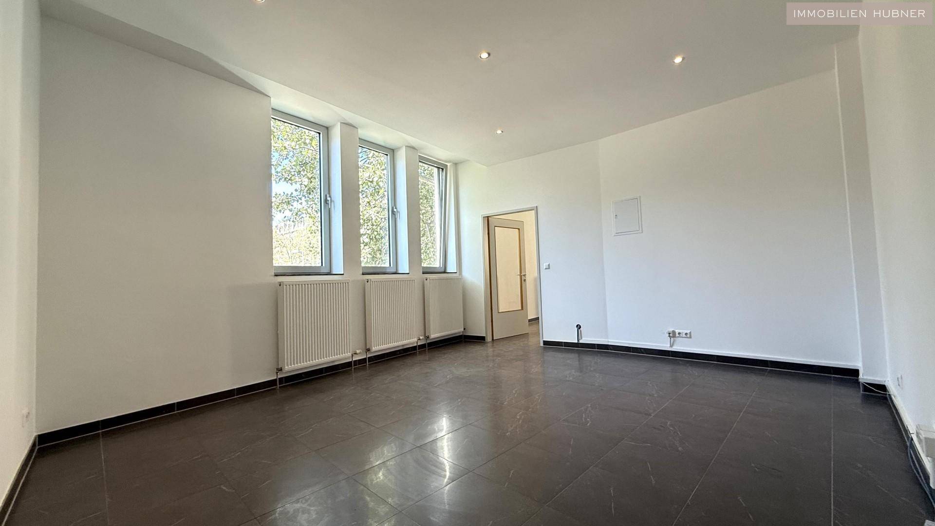 Heller Büroraum mit Fliesenboden, hohen Fenstern und einer Tür.