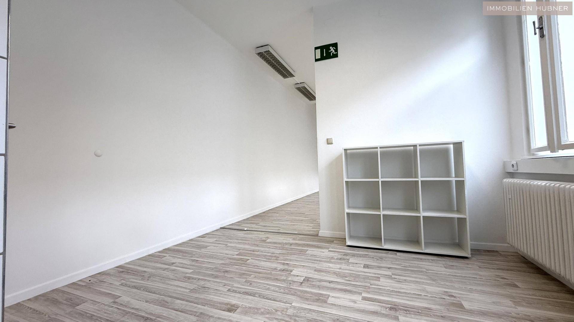 Langer Flur oder Bürobereich mit hellem Laminatboden und einem Regal an der Wand.
