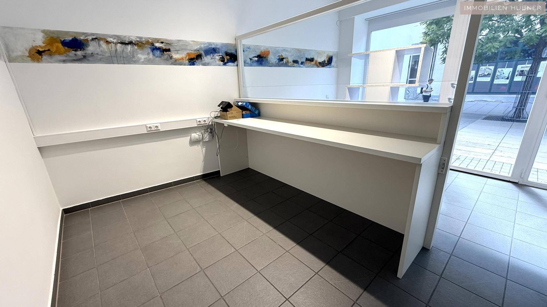 Empfangsbereich oder Theke in einem hellen Raum mit Fliesenboden und großen Fenstern.