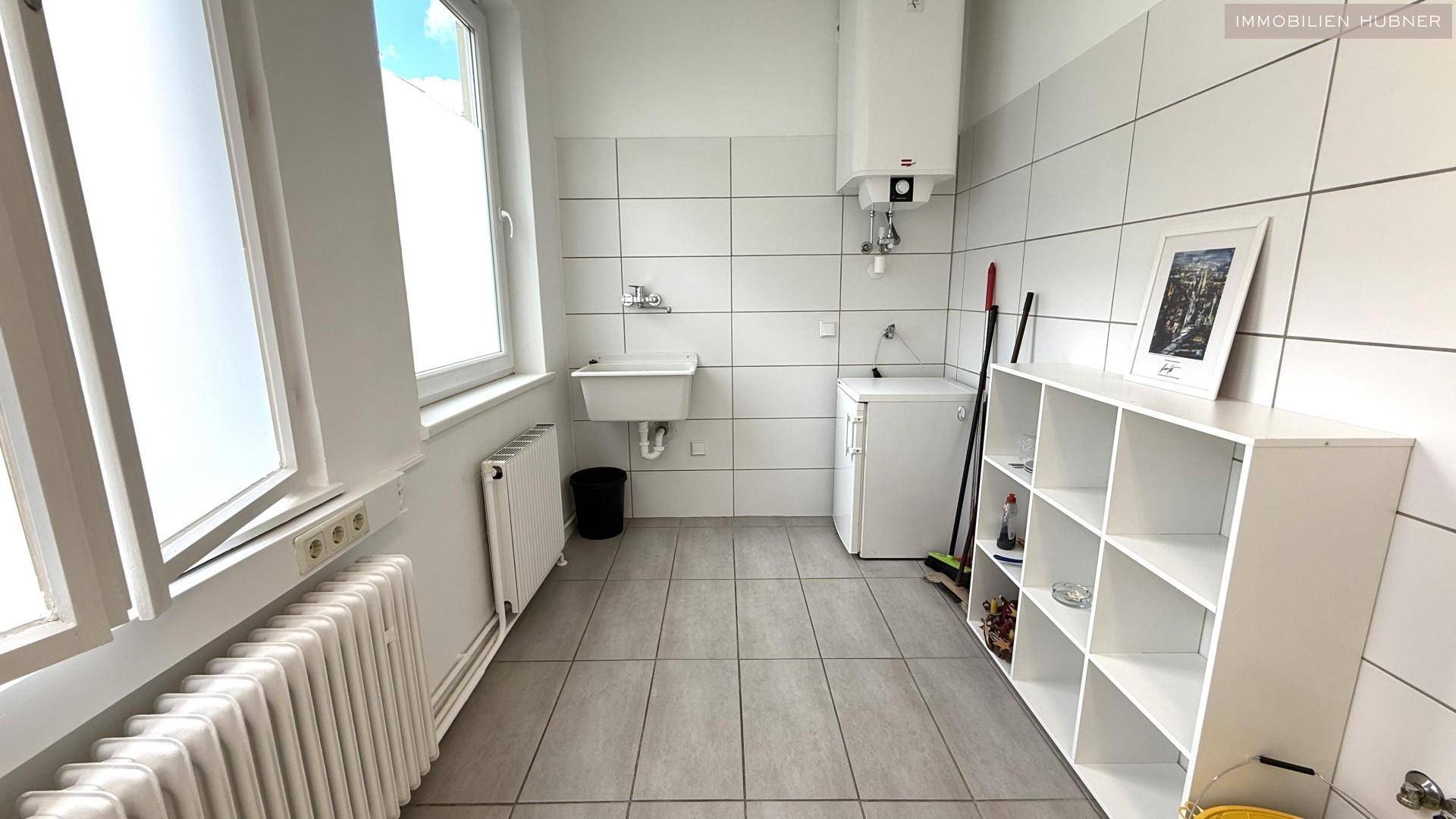 Heller Hauswirtschaftsraum mit Fliesenboden, Waschbecken, Boiler und Fenster.