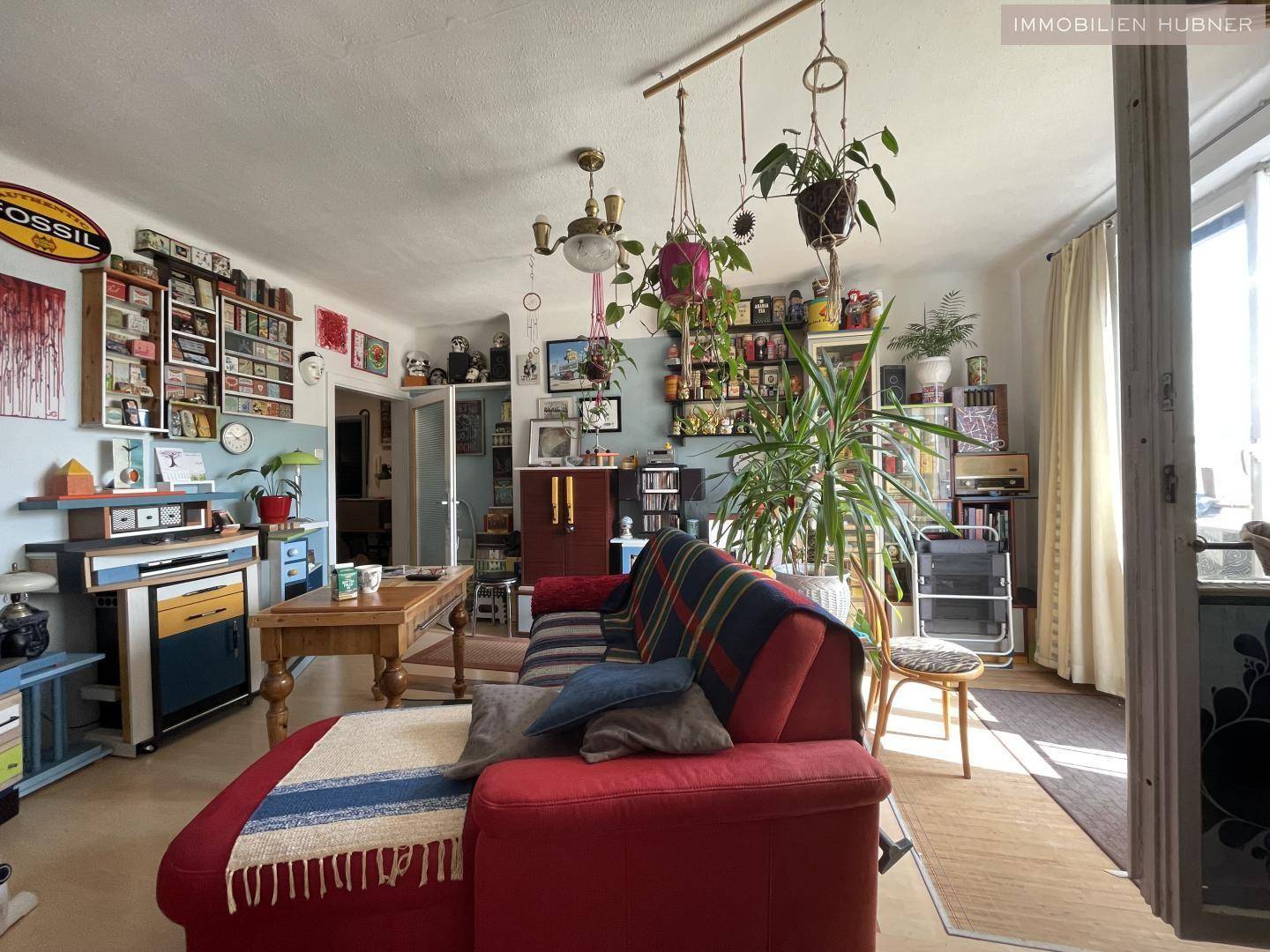 Gemütliches Wohnzimmer mit rotem Sofa, vielen Pflanzen und persönlichen Dekorationen.