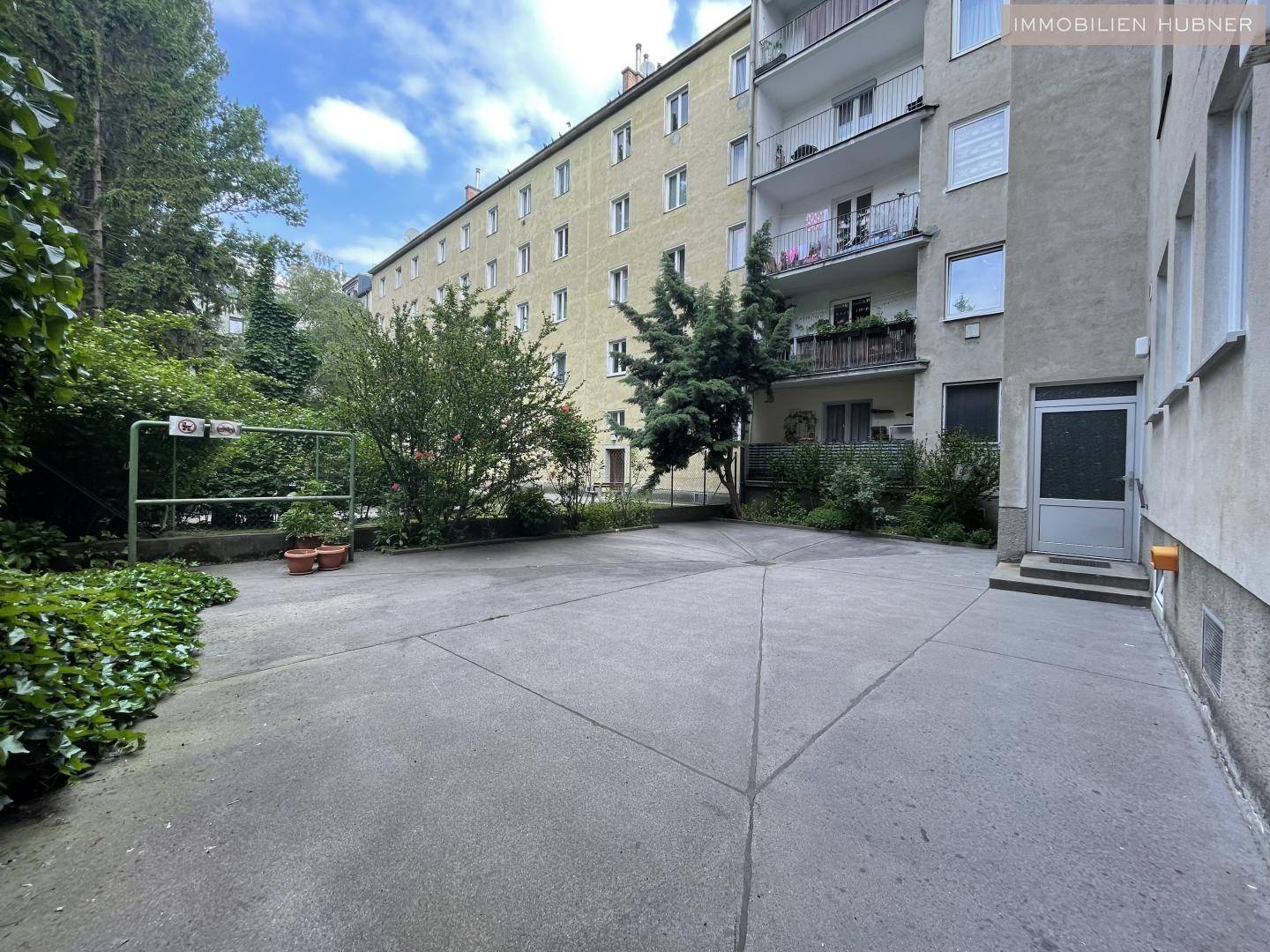 Hinterhof mit gepflasterter Fläche, umgeben von Bäumen und Sträuchern, ideal für Parkplätze.