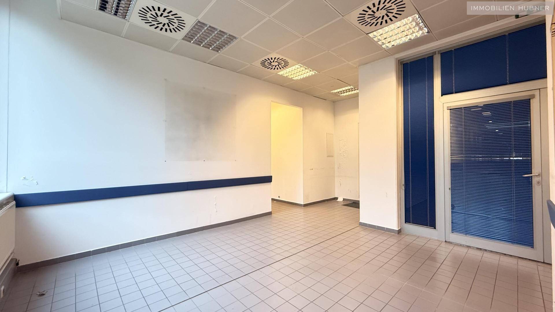 Leeres Büro mit Fliesenboden, weißen Wänden und blauen Akzenten an den Fenstern.