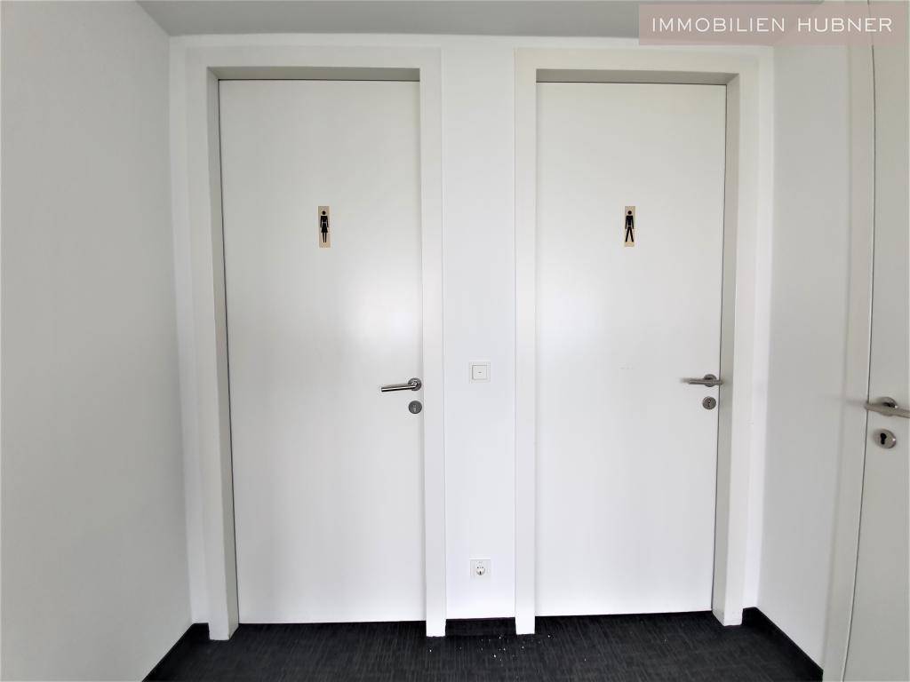 Zwei separate Toilettenkabinen mit weißen Türen und Piktogrammen in einem modernen Bürogebäude.
