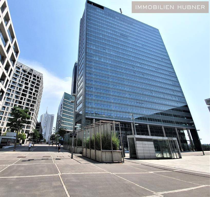 Moderne Hochhausarchitektur mit spiegelnder Glasfassade in einem städtischen Geschäftsviertel unter blauem Himmel.