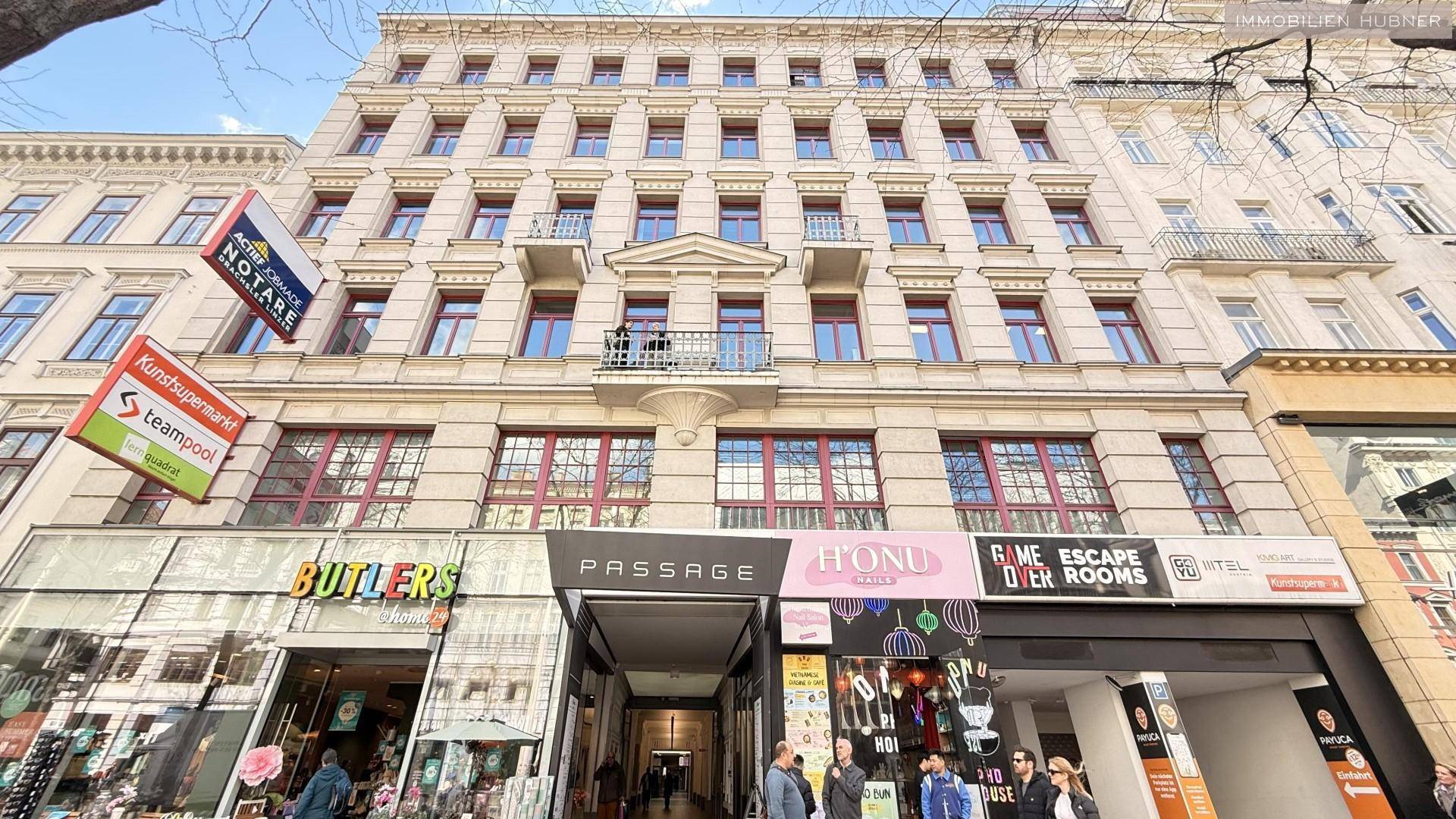 Mehrstöckiges Gebäude mit klassischer Fassade, vielen Fenstern und Geschäften im Erdgeschoss.