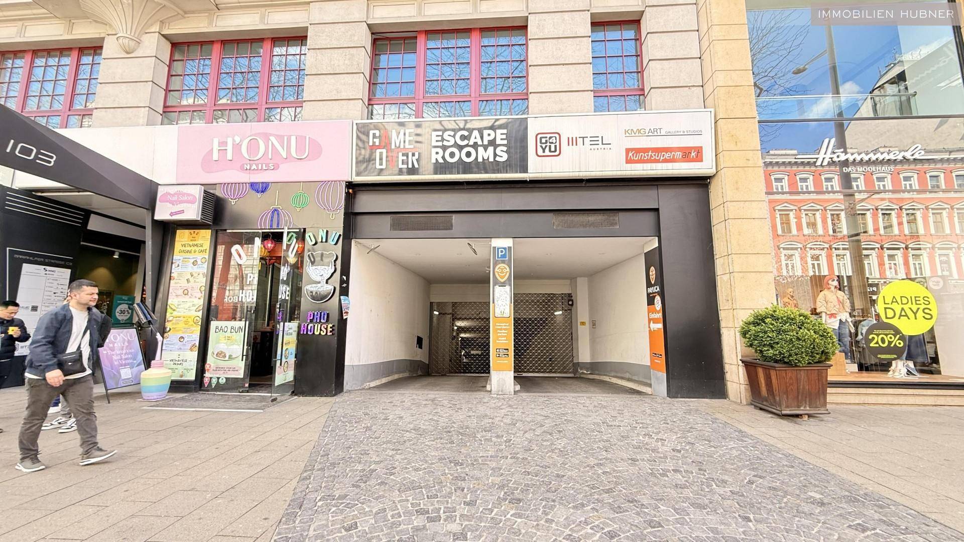 Eingangsbereich eines Gebäudes mit Geschäften und einer Einfahrt zur Tiefgarage.