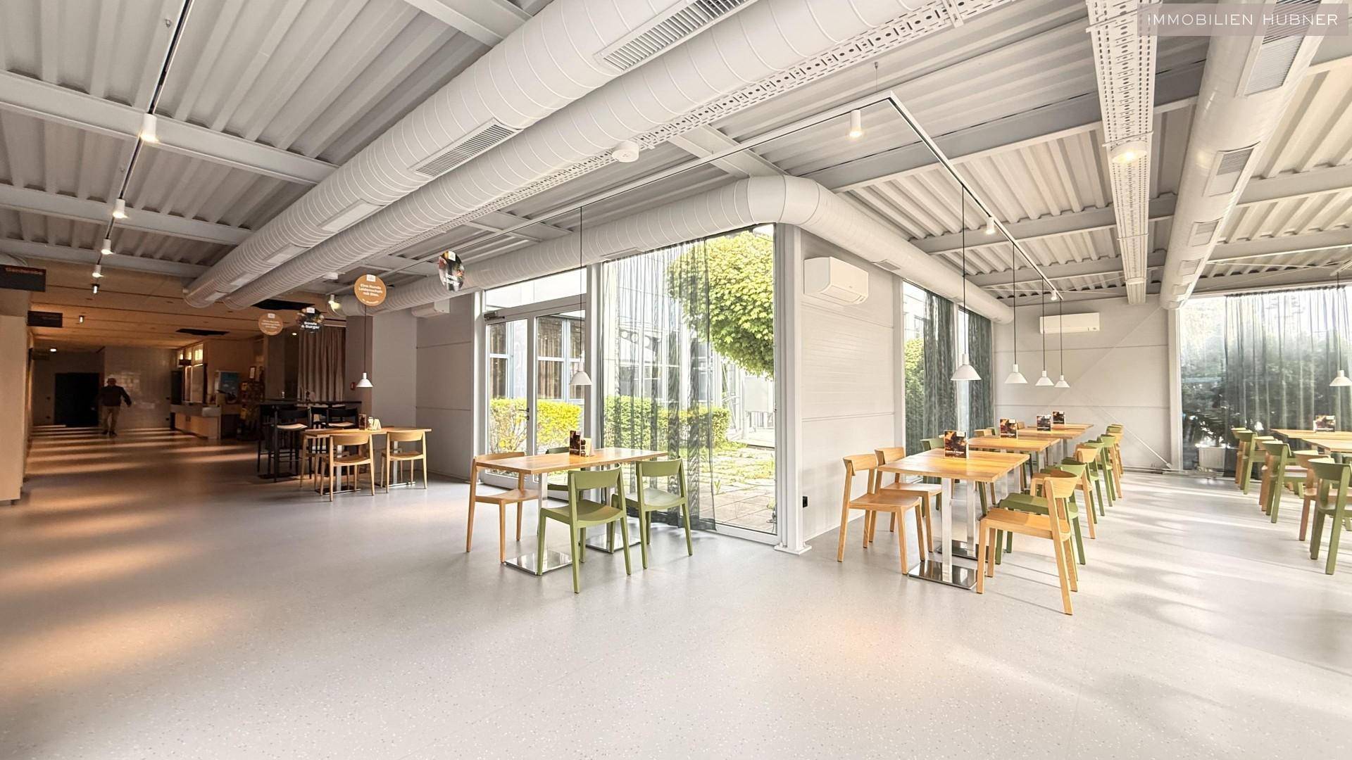 Geräumige Cafeteria mit industriellem Design, großen Fenstern und vielen Sitzgelegenheiten.