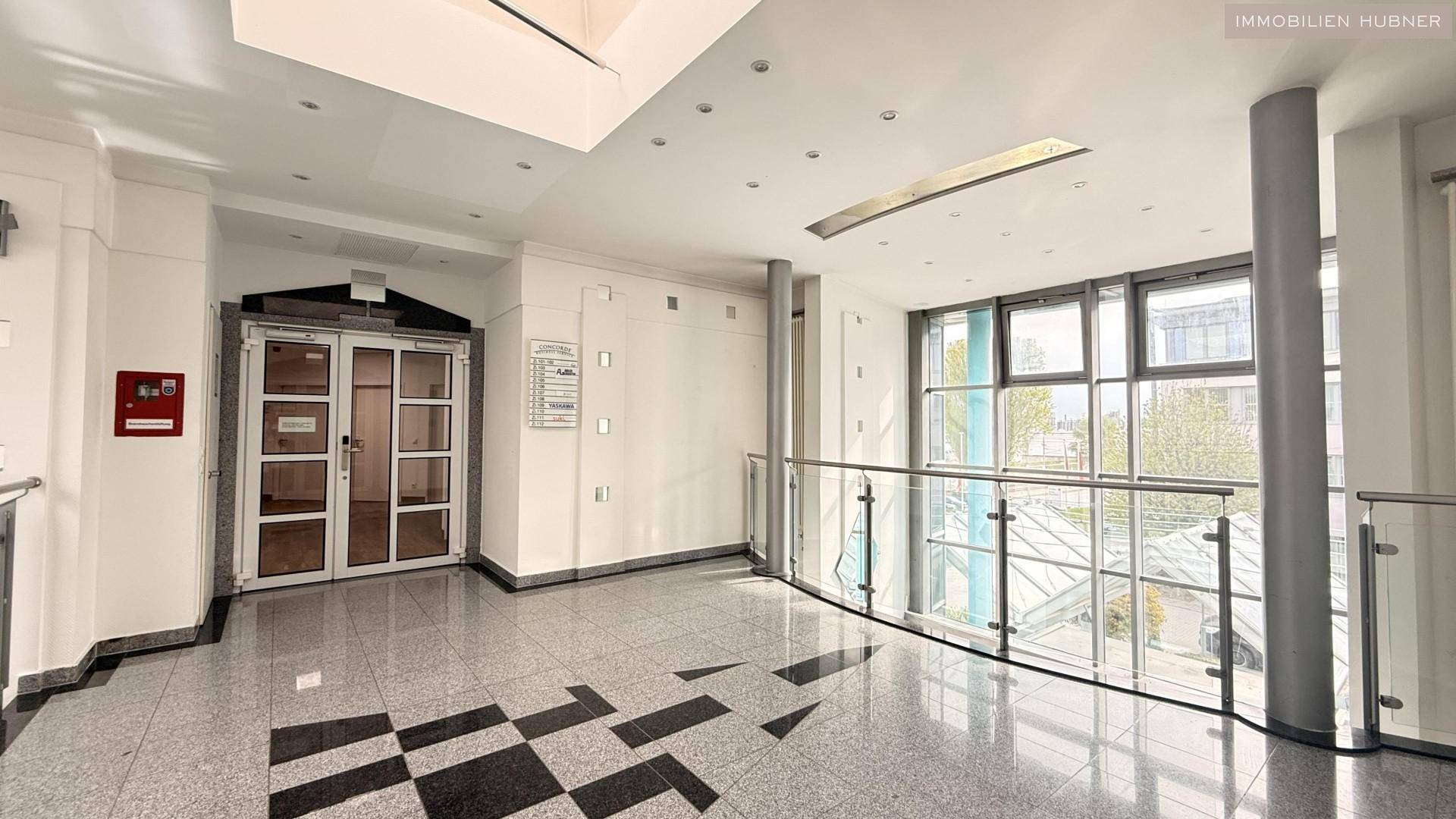 Moderne Lobby mit glänzendem Steinboden, Glasgeländer und großen Fenstern, die viel Licht spenden.
