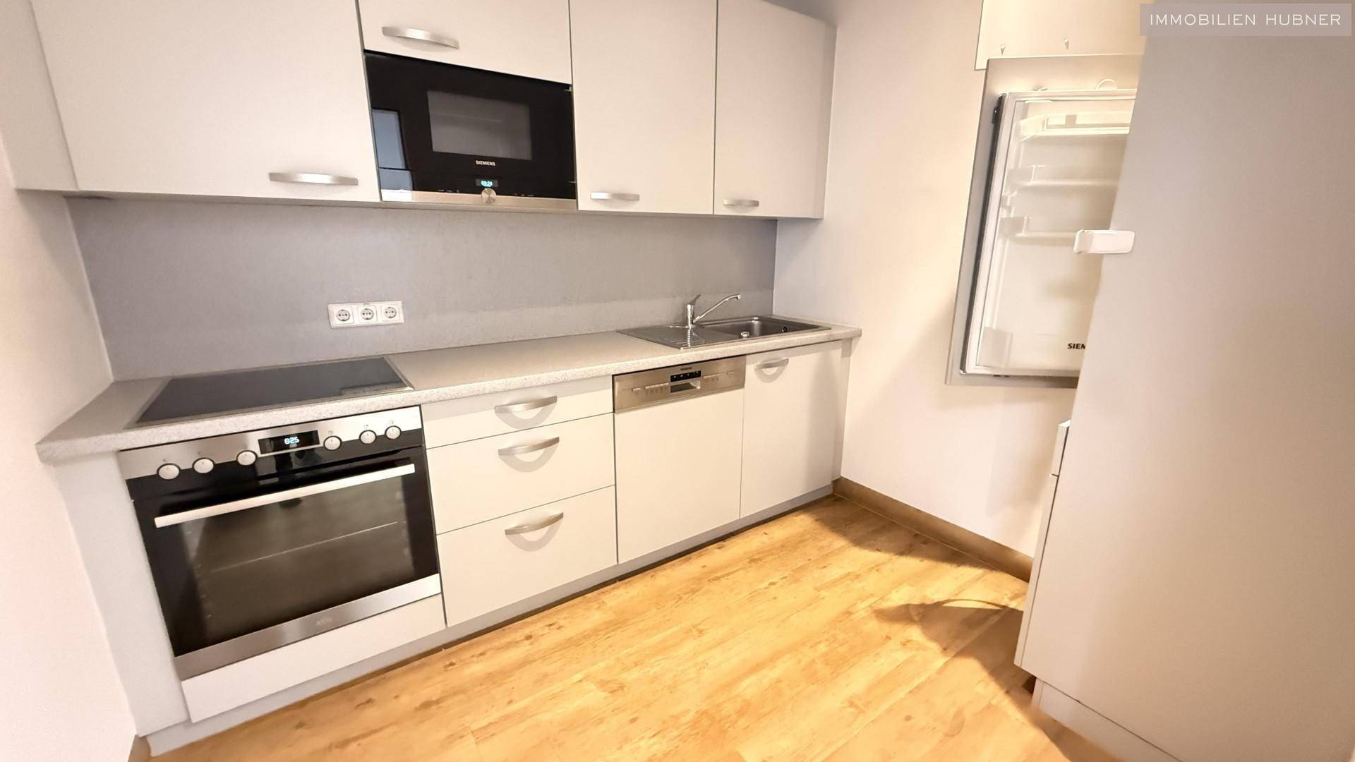 Moderne Einbauküche mit weißen Schränken, integrierten Geräten und hellem Holzoptik-Boden.