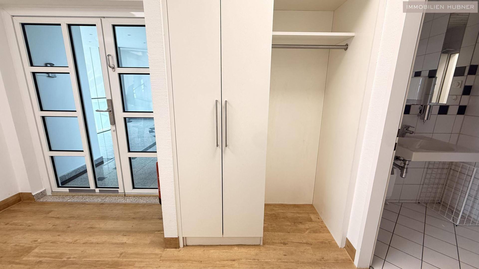Bereich mit Einbauschrank und Holzoptik-Boden, angrenzend an einen gefliesten Sanitärbereich.