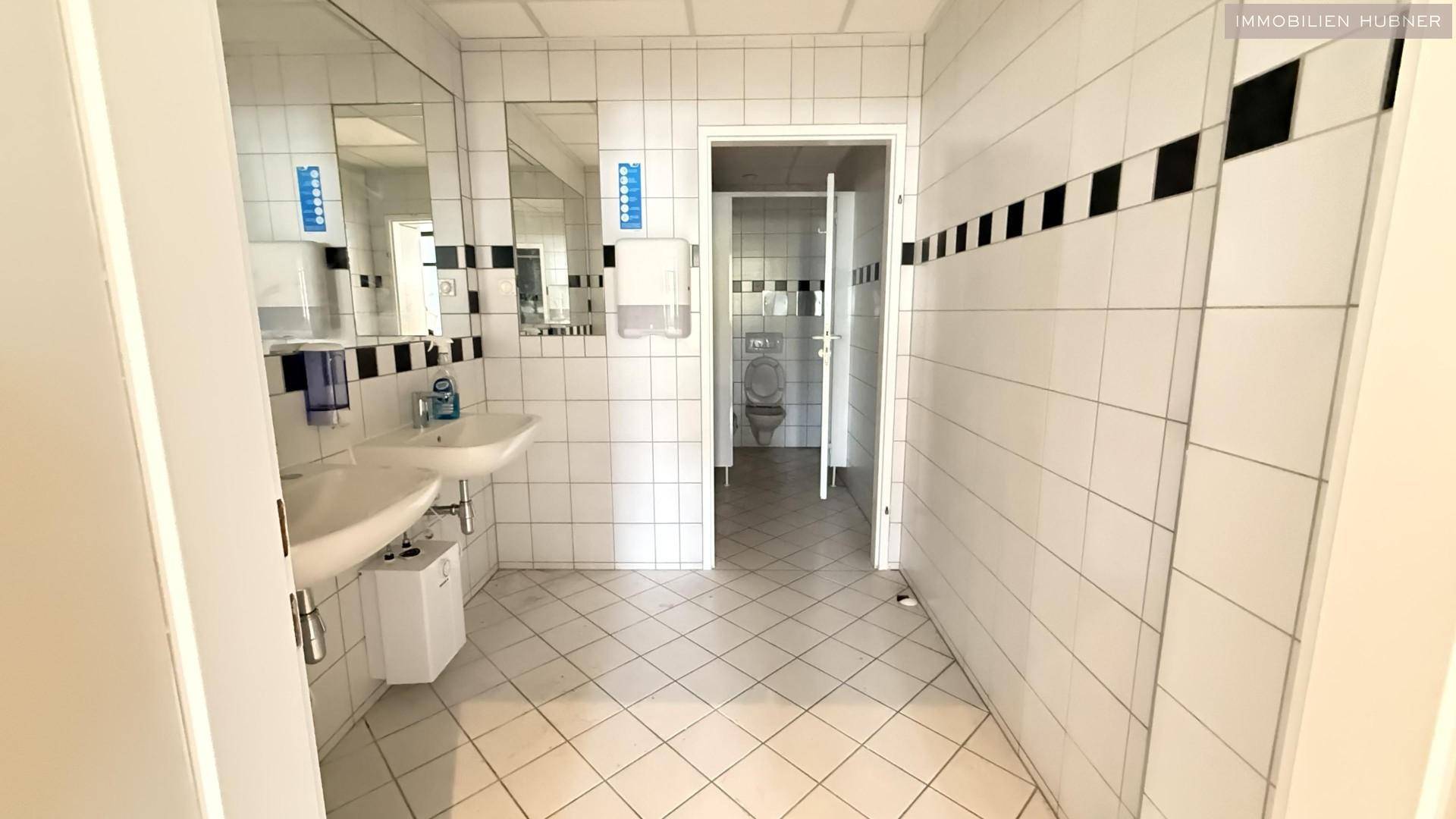 Helle, geflieste Sanitärräume mit mehreren Waschbecken und Toiletten, sauber und funktional.
