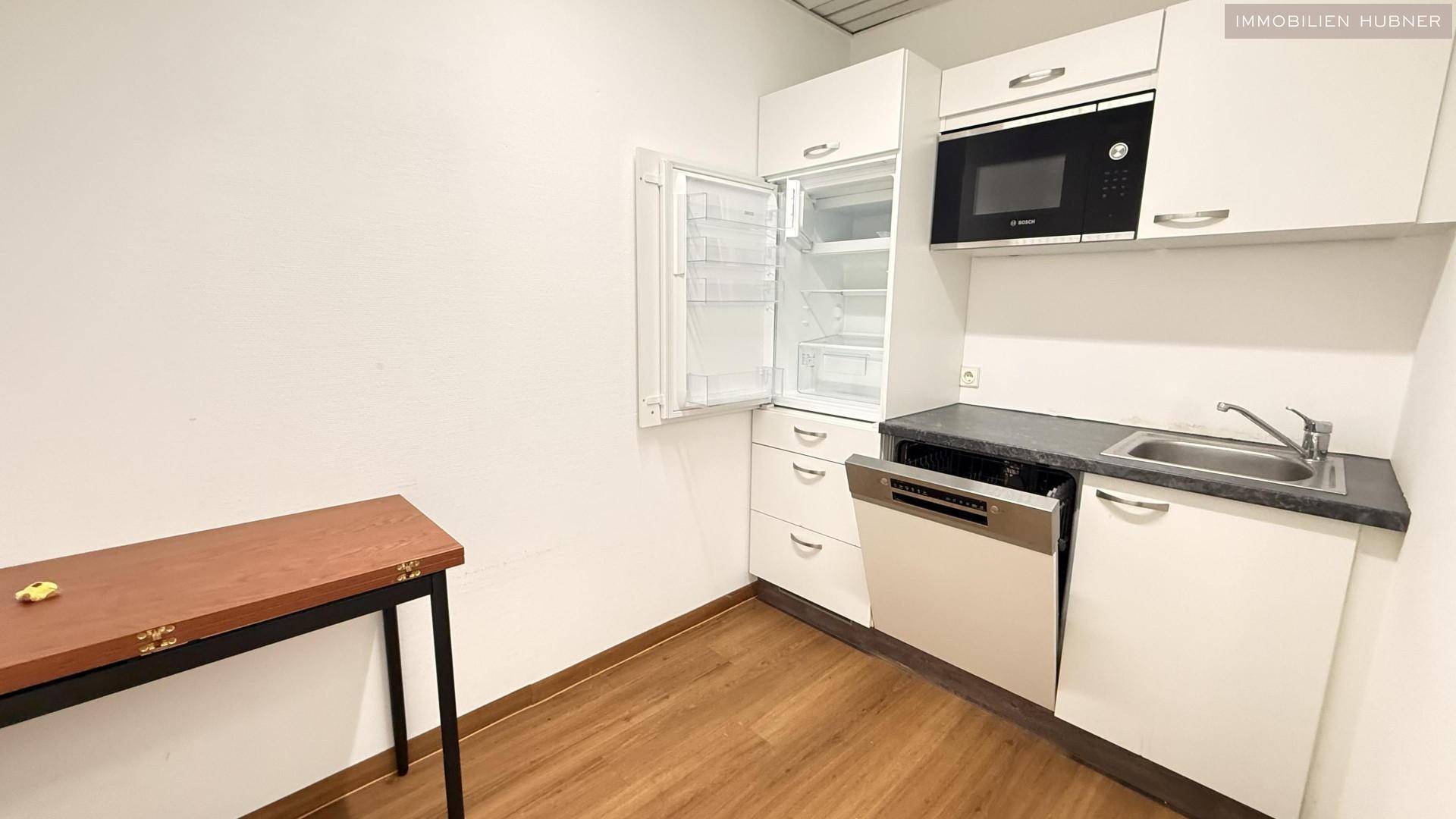 Kleine Küche mit weißen Schränken, Spüle, Kühlschrank, Mikrowelle und Geschirrspüler, ideal für Pausen.