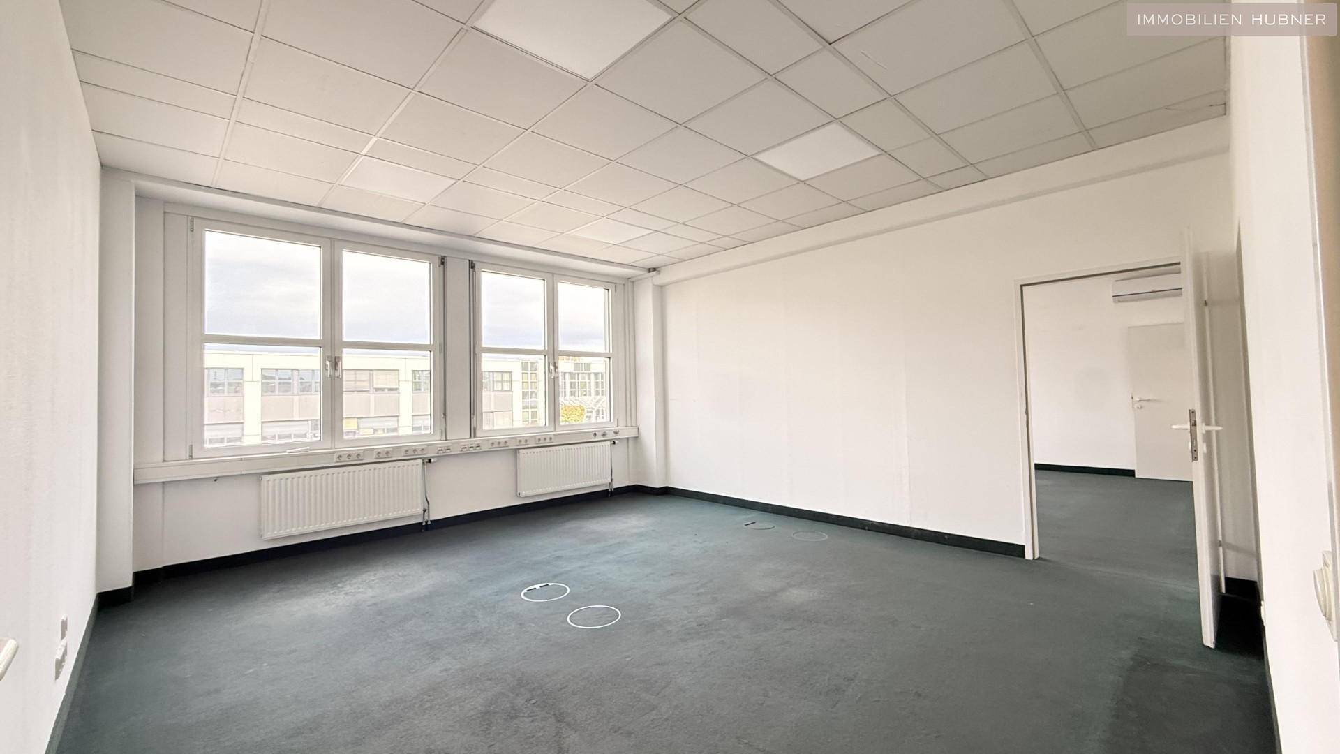Großes Büro mit Teppichboden, vielen Fenstern und Zugang zu weiteren Räumen, ideal für flexible Nutzung.