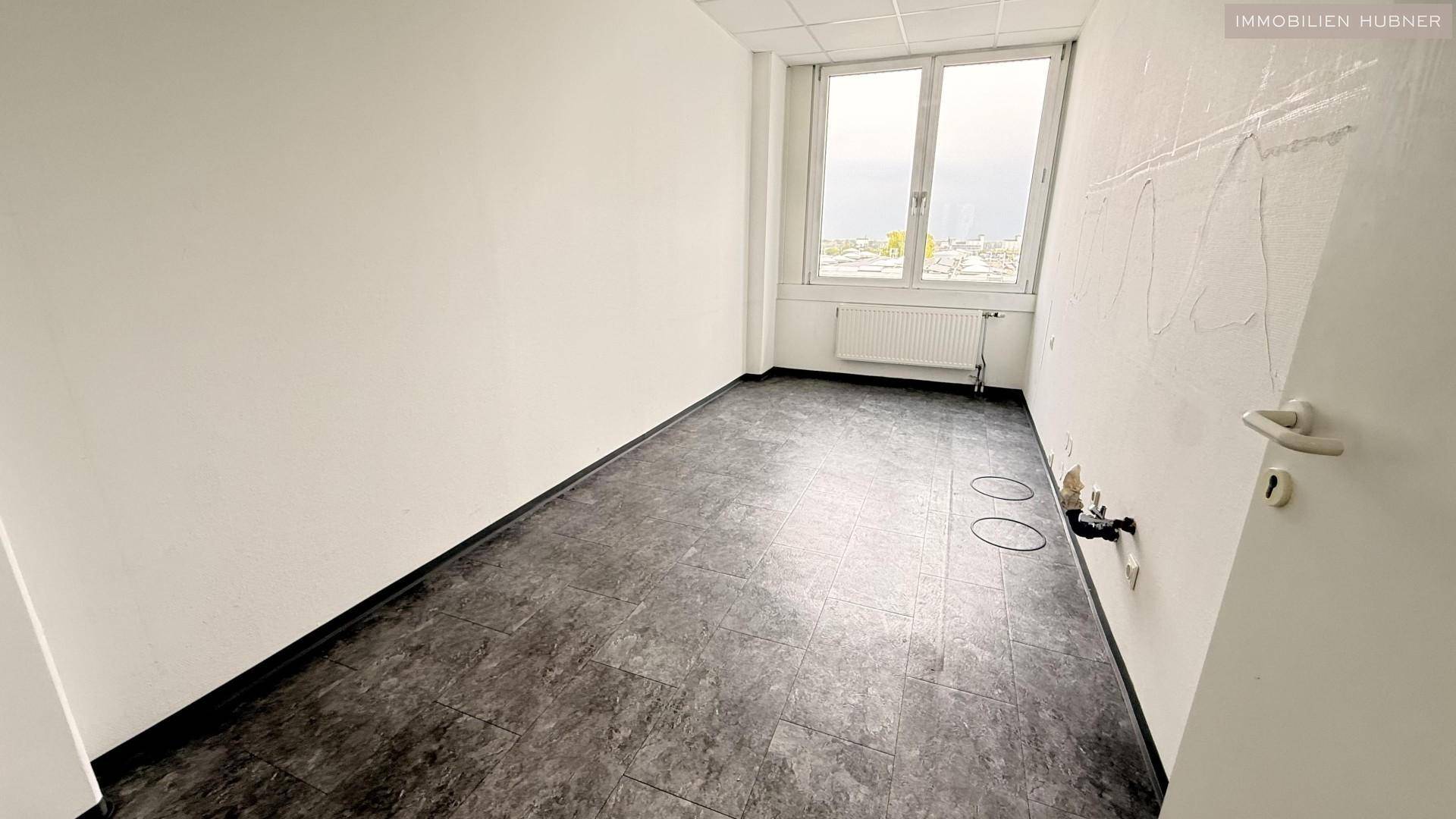 Raum mit dunklem Vinylboden und Fenster, bietet Potenzial für individuelle Nutzung oder Umbau.