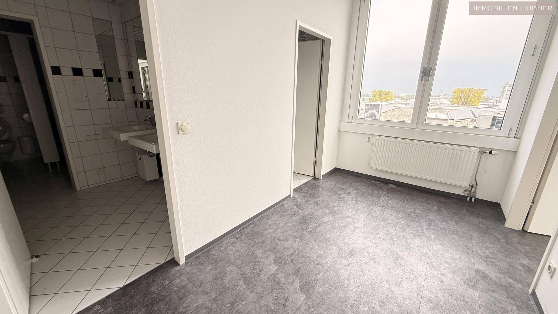 Raum mit Vinylboden und Fenster, angrenzend an ein Badezimmer mit Fliesen und Waschbecken.