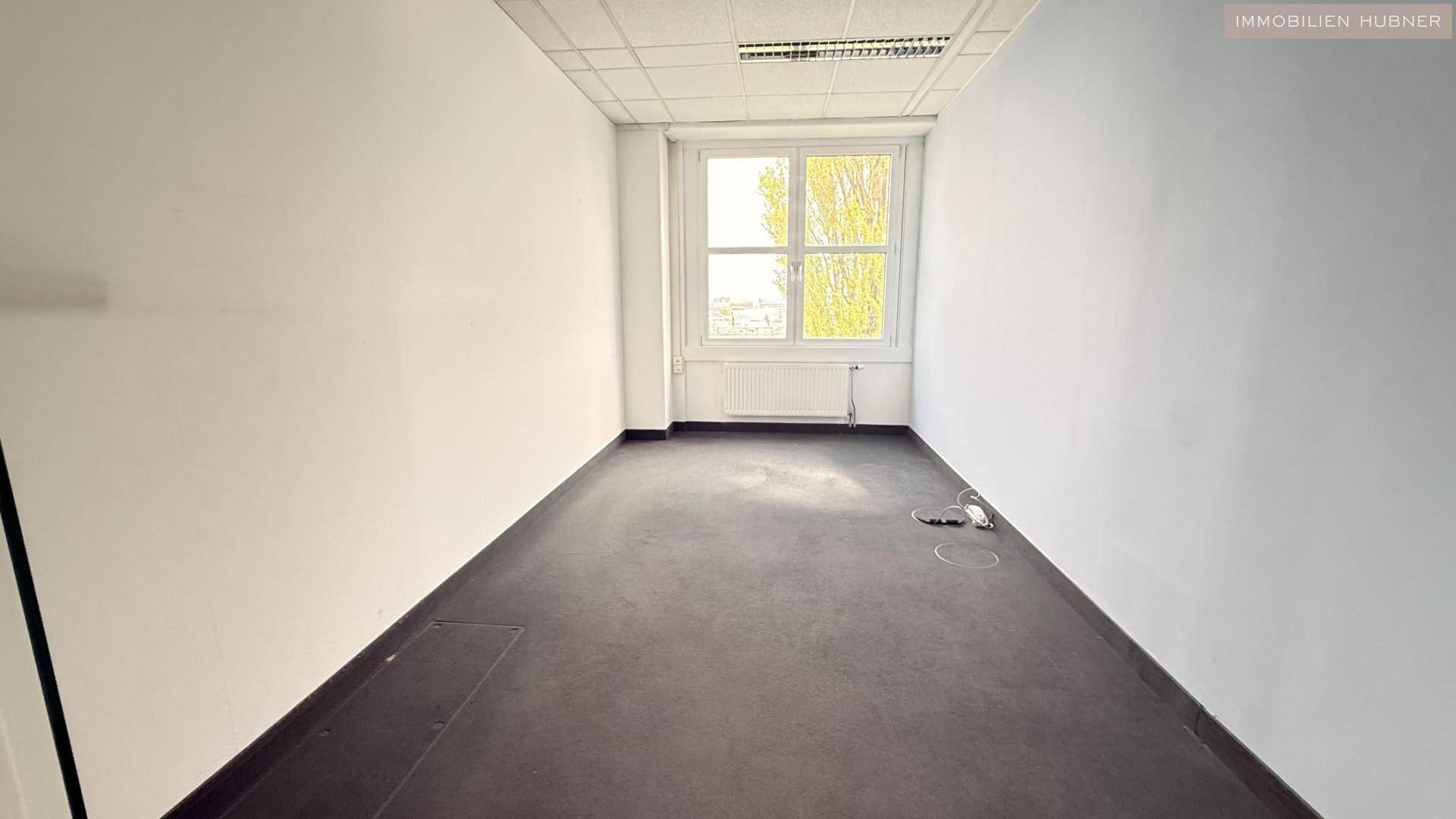 Kleineres, helles Einzelbüro mit Teppichboden und einem großen Fenster, ideal für konzentriertes Arbeiten.