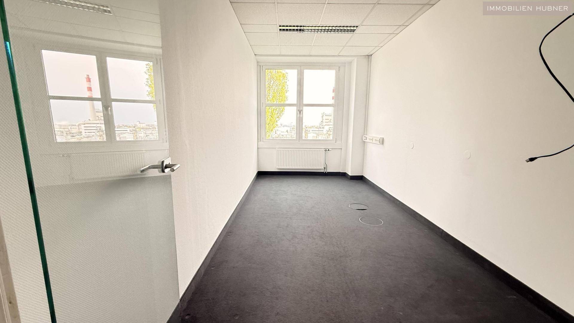 Schmaler Büroraum mit Teppichboden und einem Fenster, das Tageslicht hereinlässt, ideal für ein Einzelbüro.