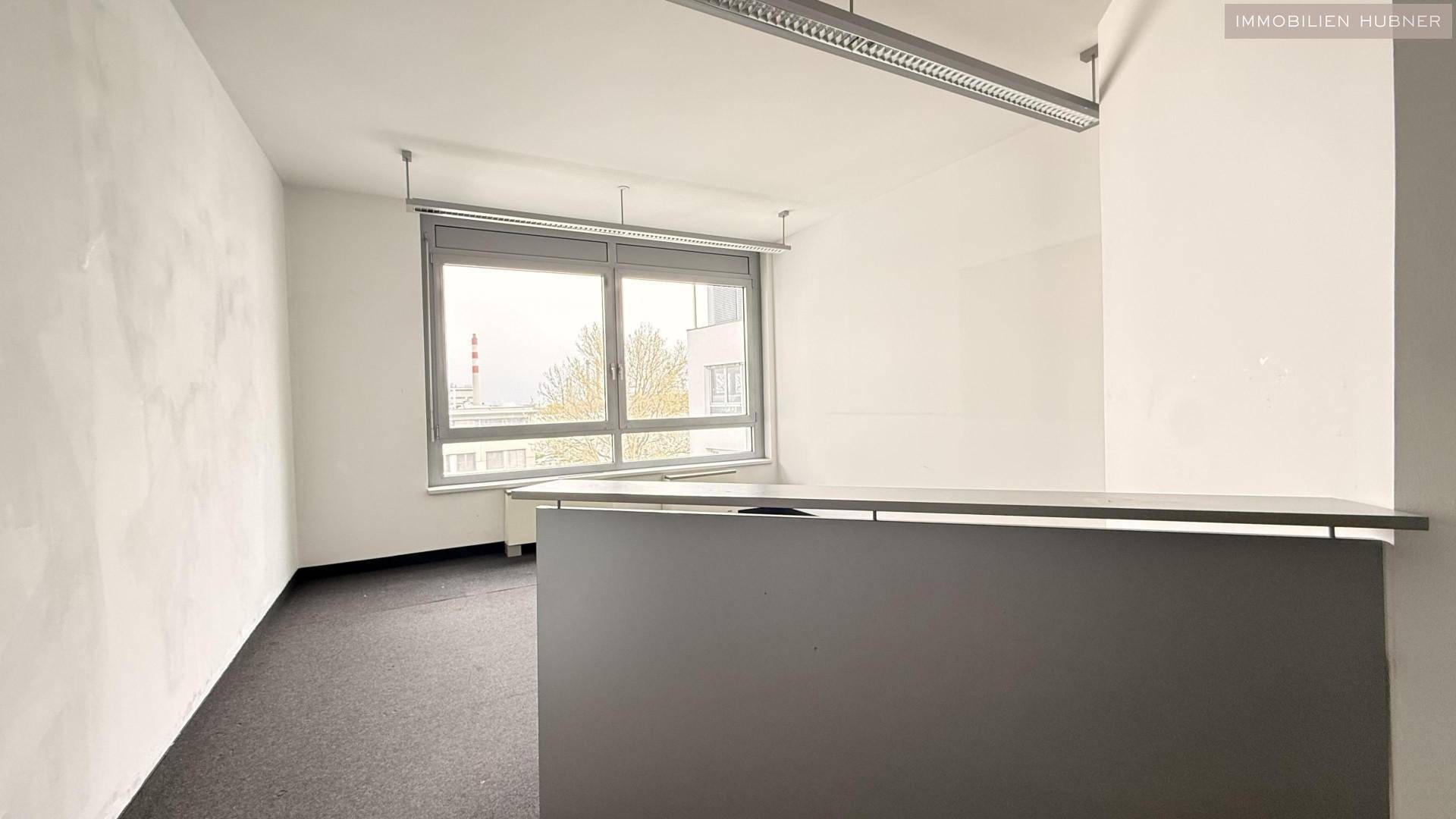 Büroraum mit Empfangstheke, Teppichboden und großen Fenstern für viel Licht, ideal für Kundenempfang.