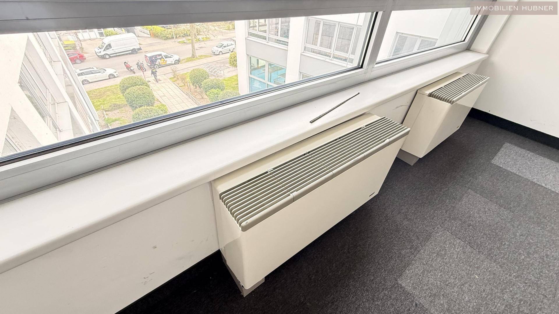 Große Fensterfront mit Heizkörpern und Blick auf die Außenanlage, sorgt für angenehmes Raumklima.