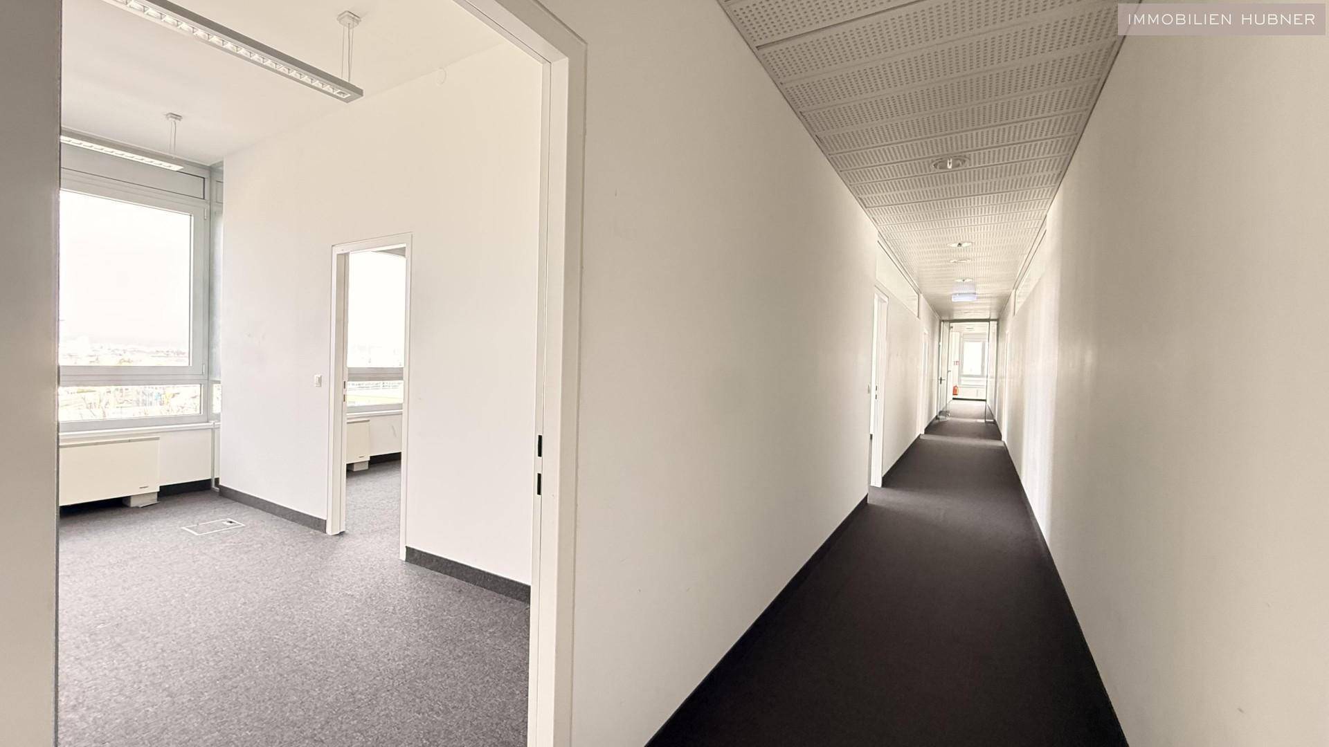 Heller Flur mit Teppichboden und Blick in einen angrenzenden Büroraum, gut gepflegt.