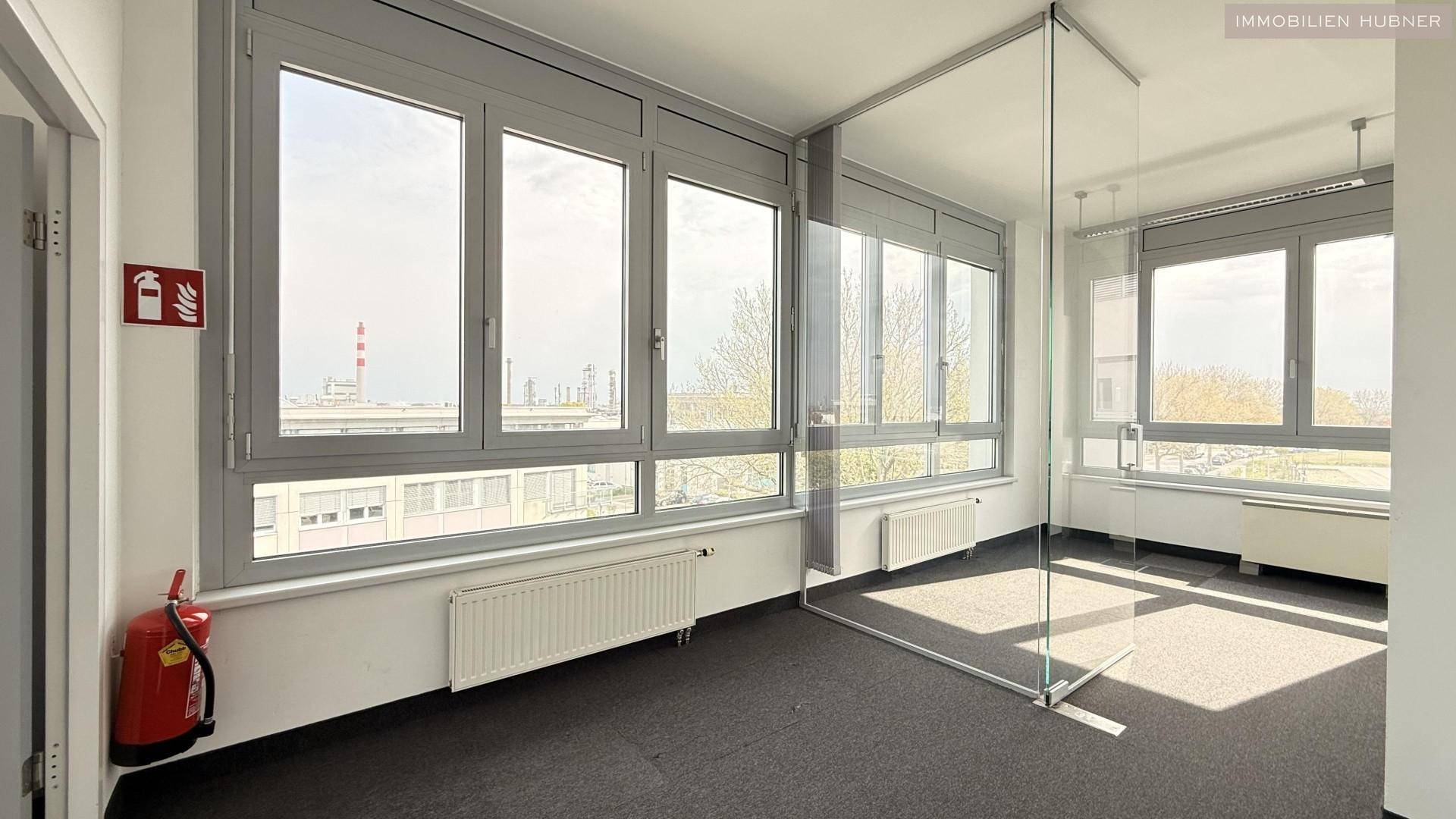 Heller Büroraum mit großen Fenstern, Glaswand und Blick auf die Umgebung, schafft eine offene Arbeitsumgebung.