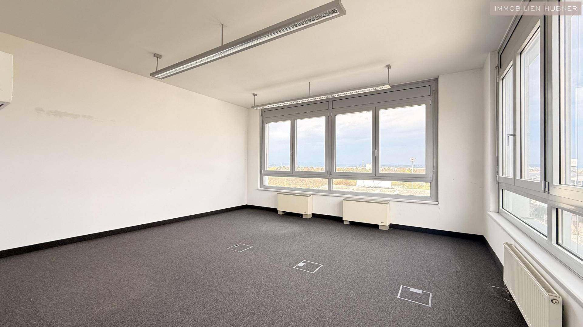 Leerer Büroraum mit Teppichboden, großen Fenstern und Bodentanks für Anschlüsse, flexibel nutzbar.