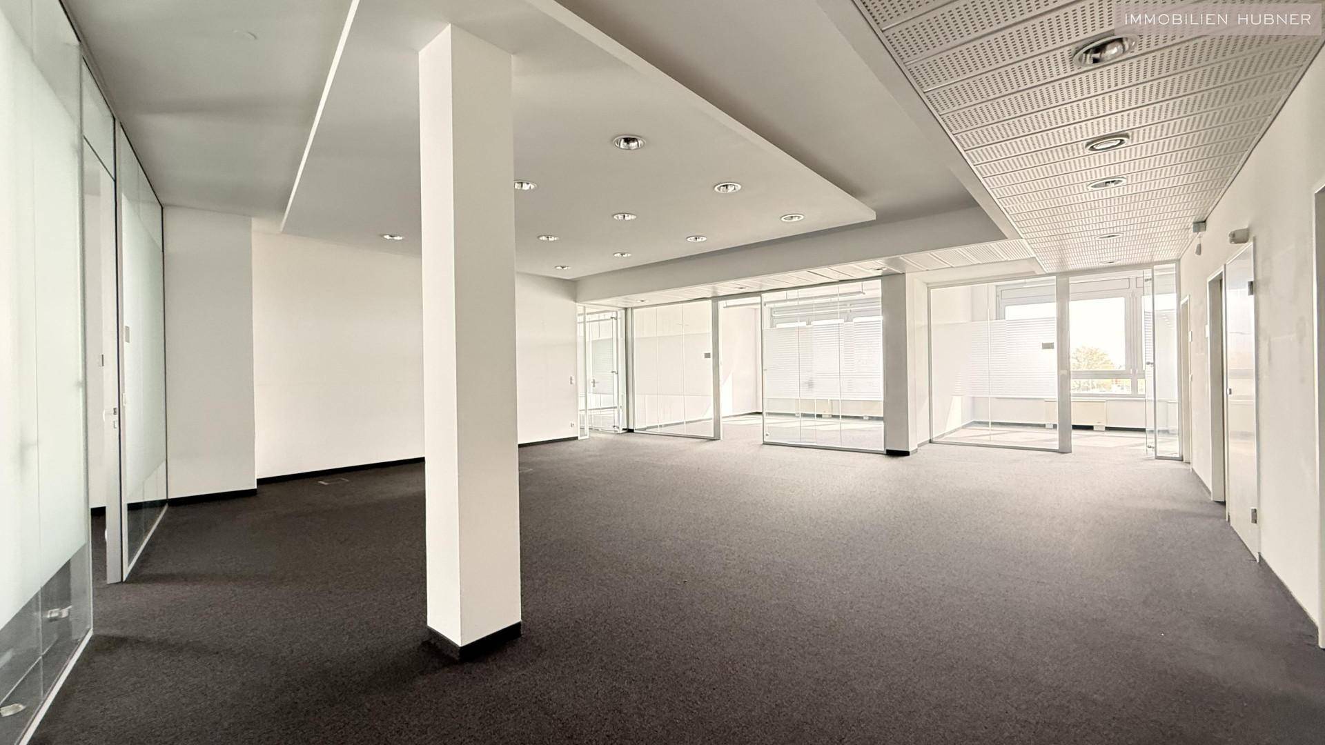 Weitläufiger Büroraum mit Säule, Teppichboden und Glaswänden, ideal für Großraumbüros.