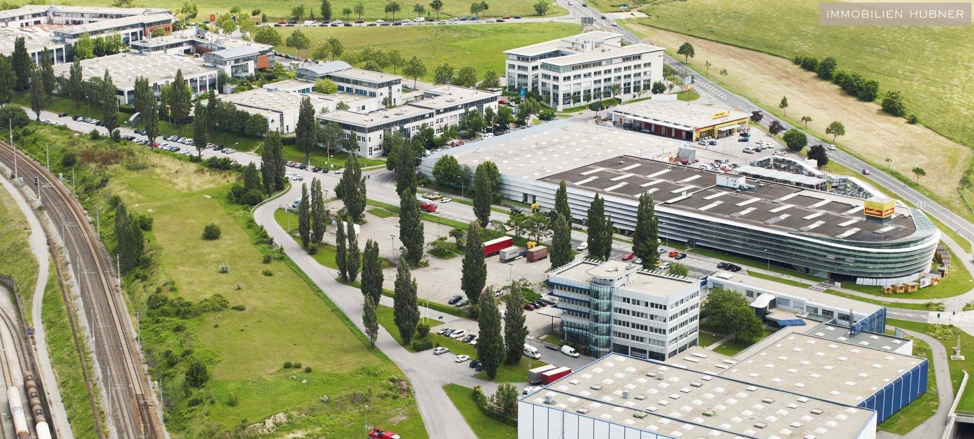 Luftaufnahme eines Gewerbegebiets mit mehreren Gebäuden, Parkplätzen und viel Grün.
