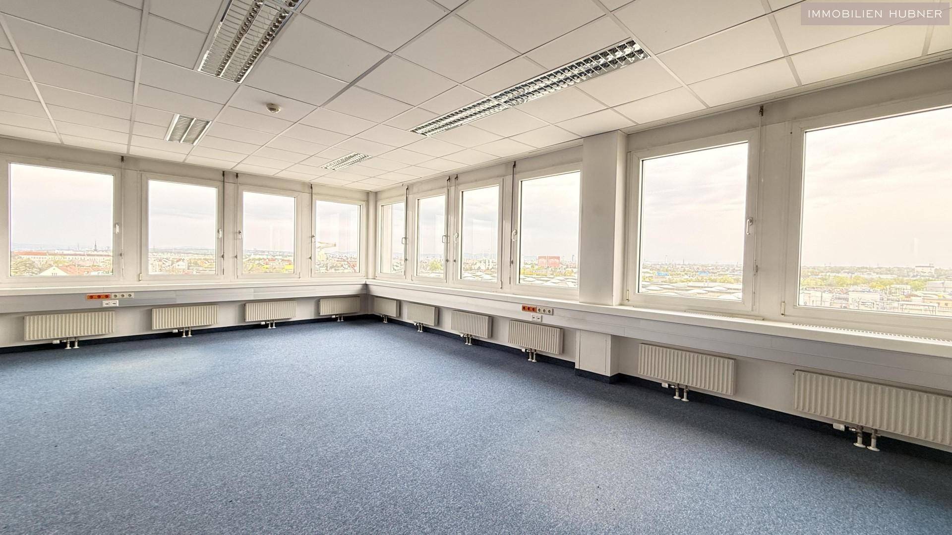 Helles Büro mit blauer Teppichboden, vielen Fenstern und Panoramablick auf die Stadt.