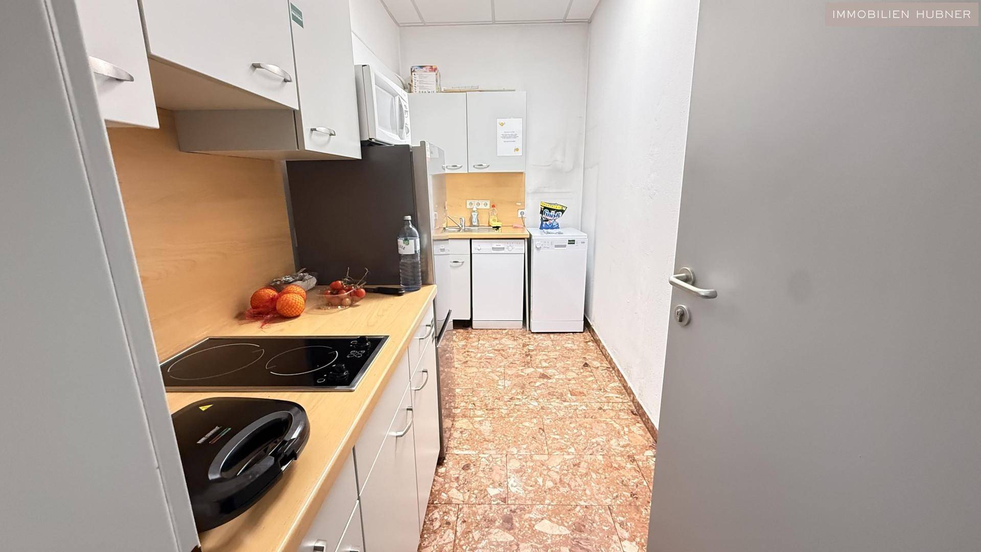 Kleine Küchenzeile mit Spüle, Kochfeld, Mikrowelle und Kühlschrank in einem Bürogebäude.