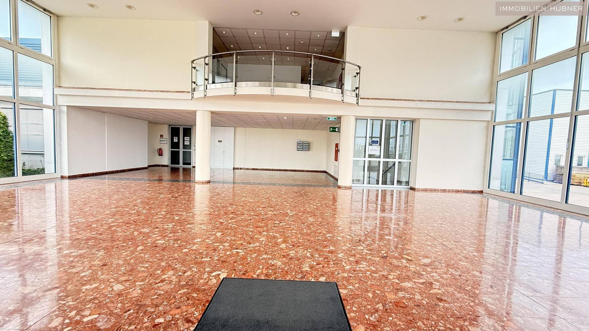 Heller Eingangsbereich mit glänzendem Terrazzoboden und einer Galerie im Obergeschoss.