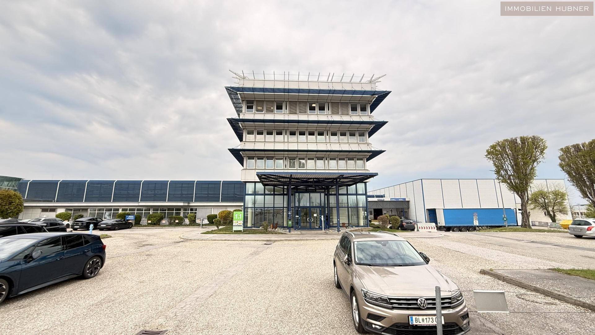 Modernes Bürogebäude mit gestufter Architektur und großem Parkplatz, umgeben von weiteren Gewerbebauten.