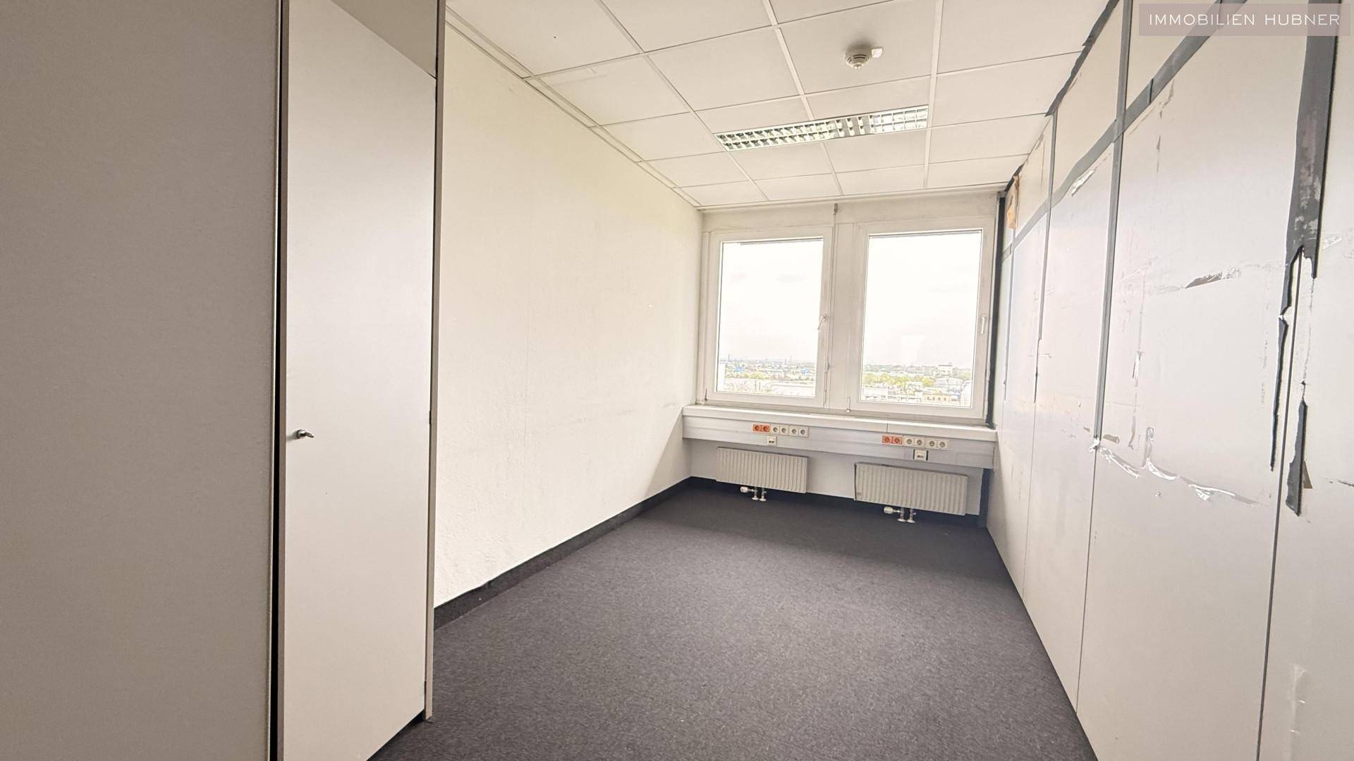 Kompaktes Büro mit Teppichboden, zwei Fenstern und praktischen Einbauschränken, gut für konzentriertes Arbeiten.